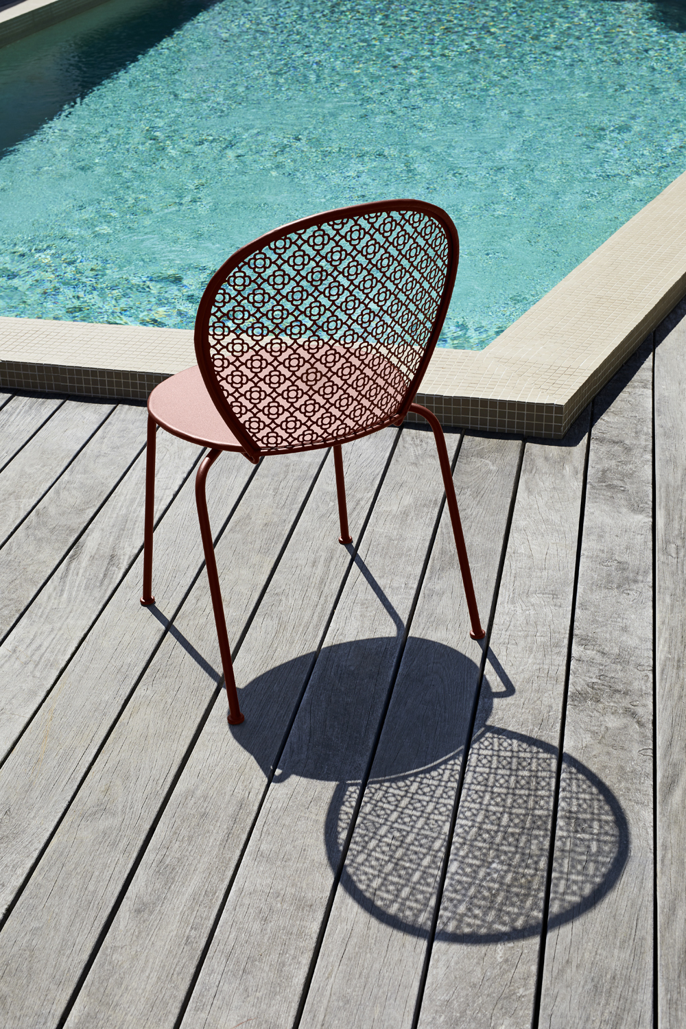Lorette Stuhl von Fermob in Rotbraun auf Holzdeck neben Pool. Outdoor Möbel.