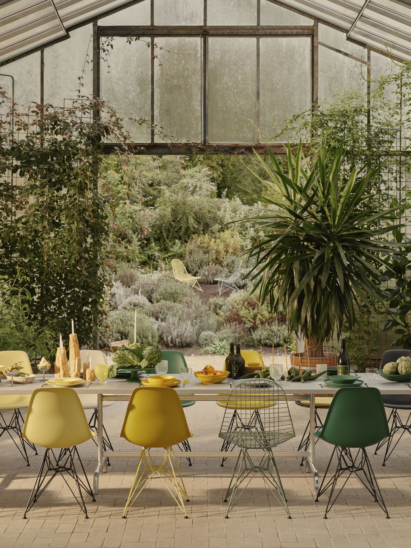 Esstisch im Gewächshaus mit Vitra Eames Fiberglass Chairs in Gelb, Grün und Grau.