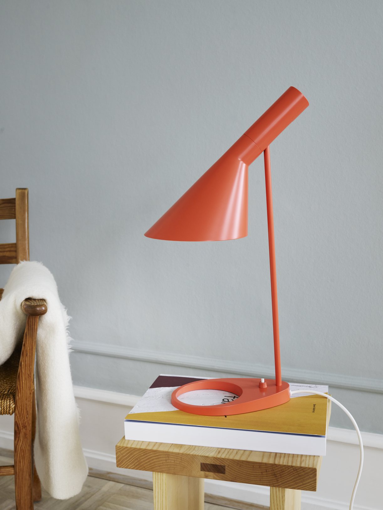 Orangefarbene AJ Tischleuchte von Louis Poulsen auf einem Stapel Bücher, modernes Design.