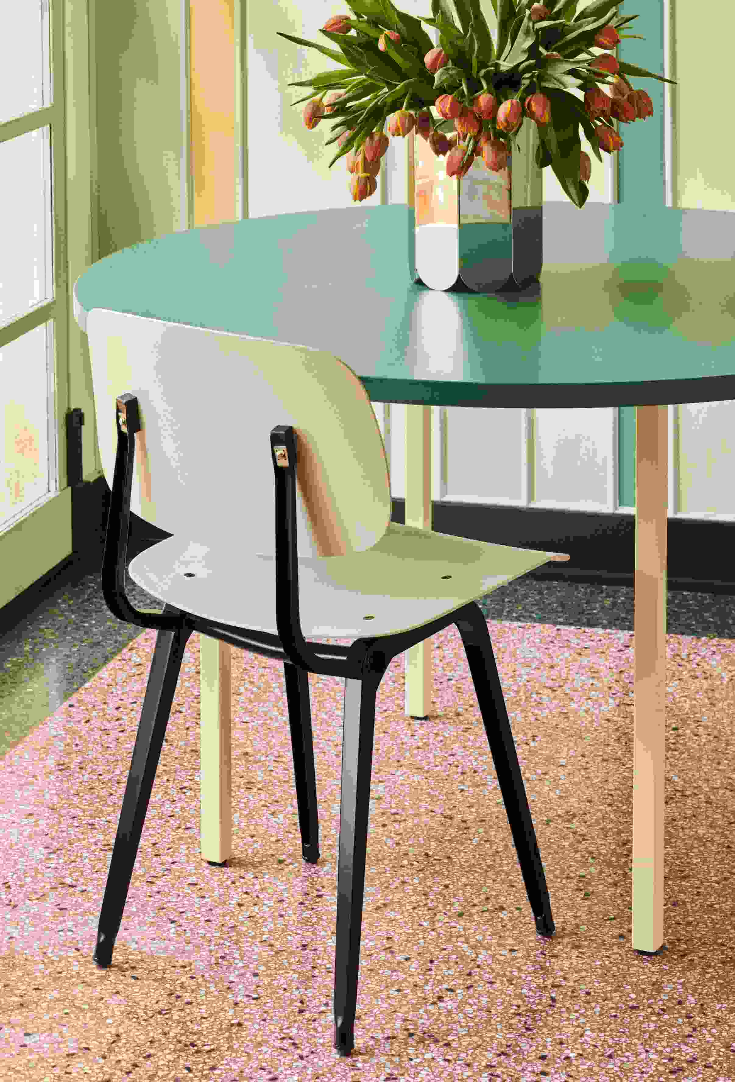 Arcs Vase L Mirror von Hay mit Tulpen auf einem runden Tisch neben einem Stuhl.