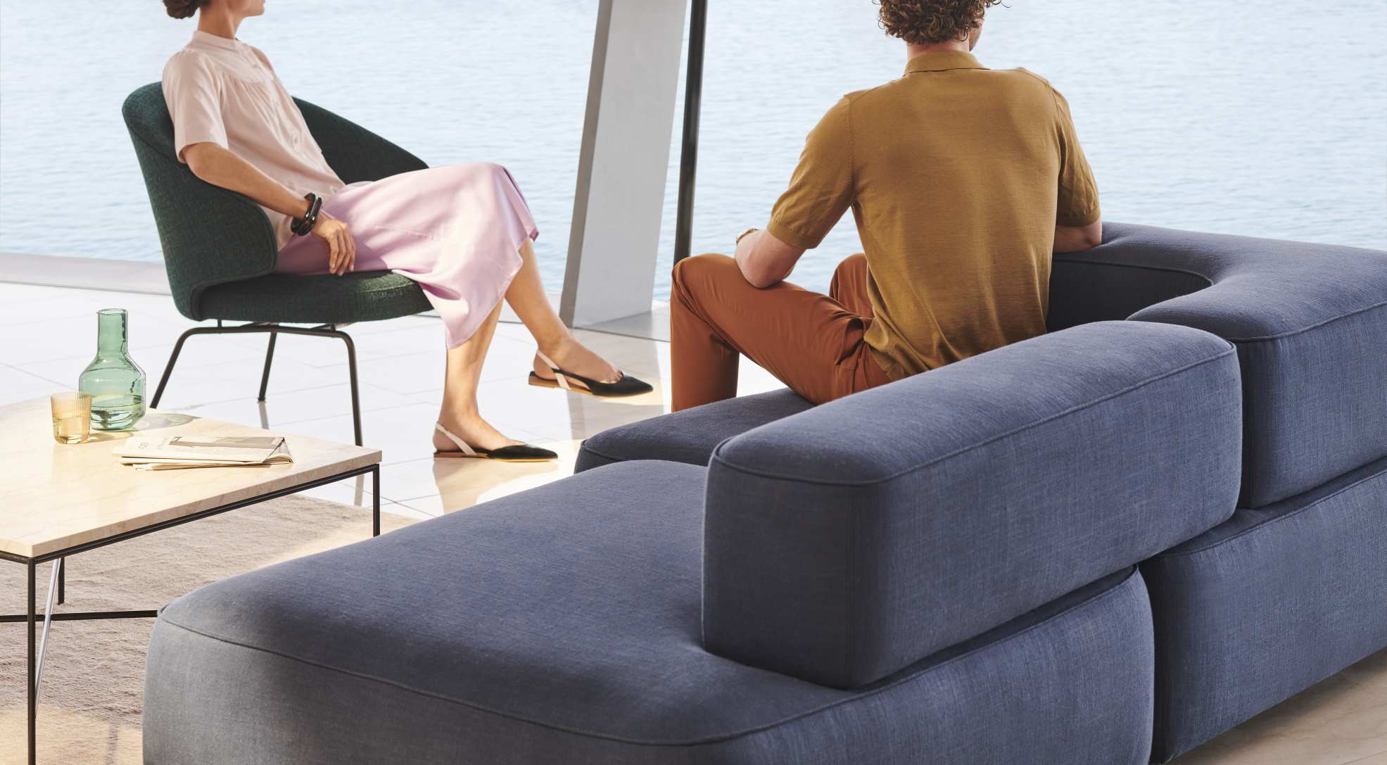 Person sitzt im Fritz Hansen Let Sessel und eine weitere Person auf einem modularen Sofa.