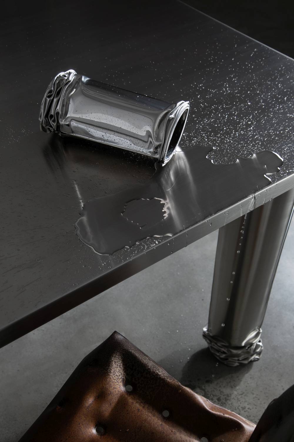 Detailaufnahme des Crash Table Esstisch Zieta mit Wasser und einem umgekippten, verformten Becher.