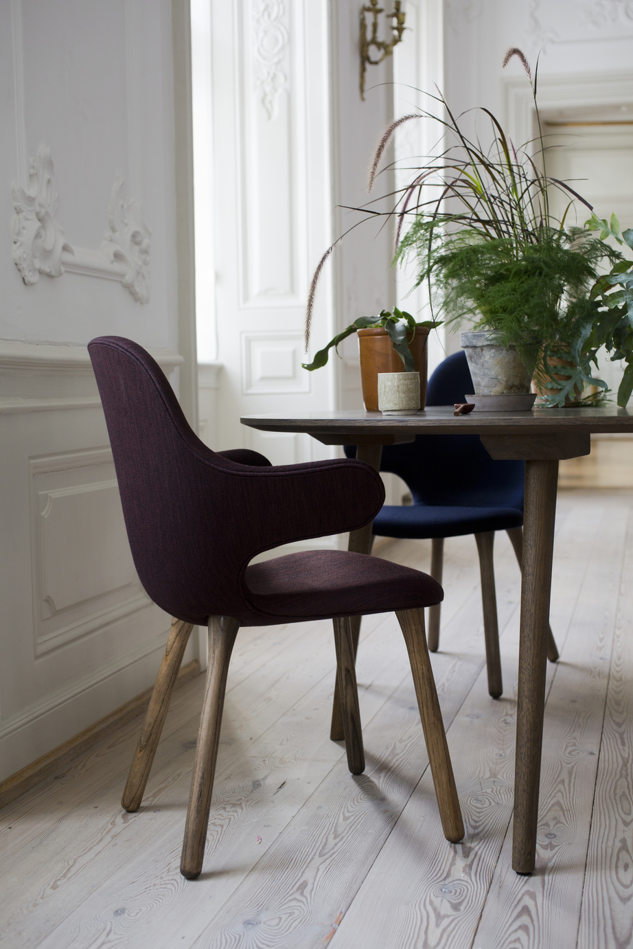 Nahaufnahme eines burgunderroten Catch Chair Stuhls von AndTradition mit Holzbeinen am Esstisch.