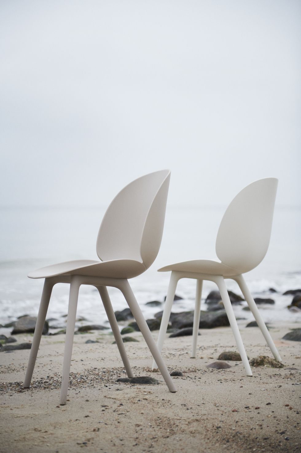 Zwei beigefarbene Beetle Chair Outdoor Esszimmerstühle von Gubi am Strand vor dem Meer.