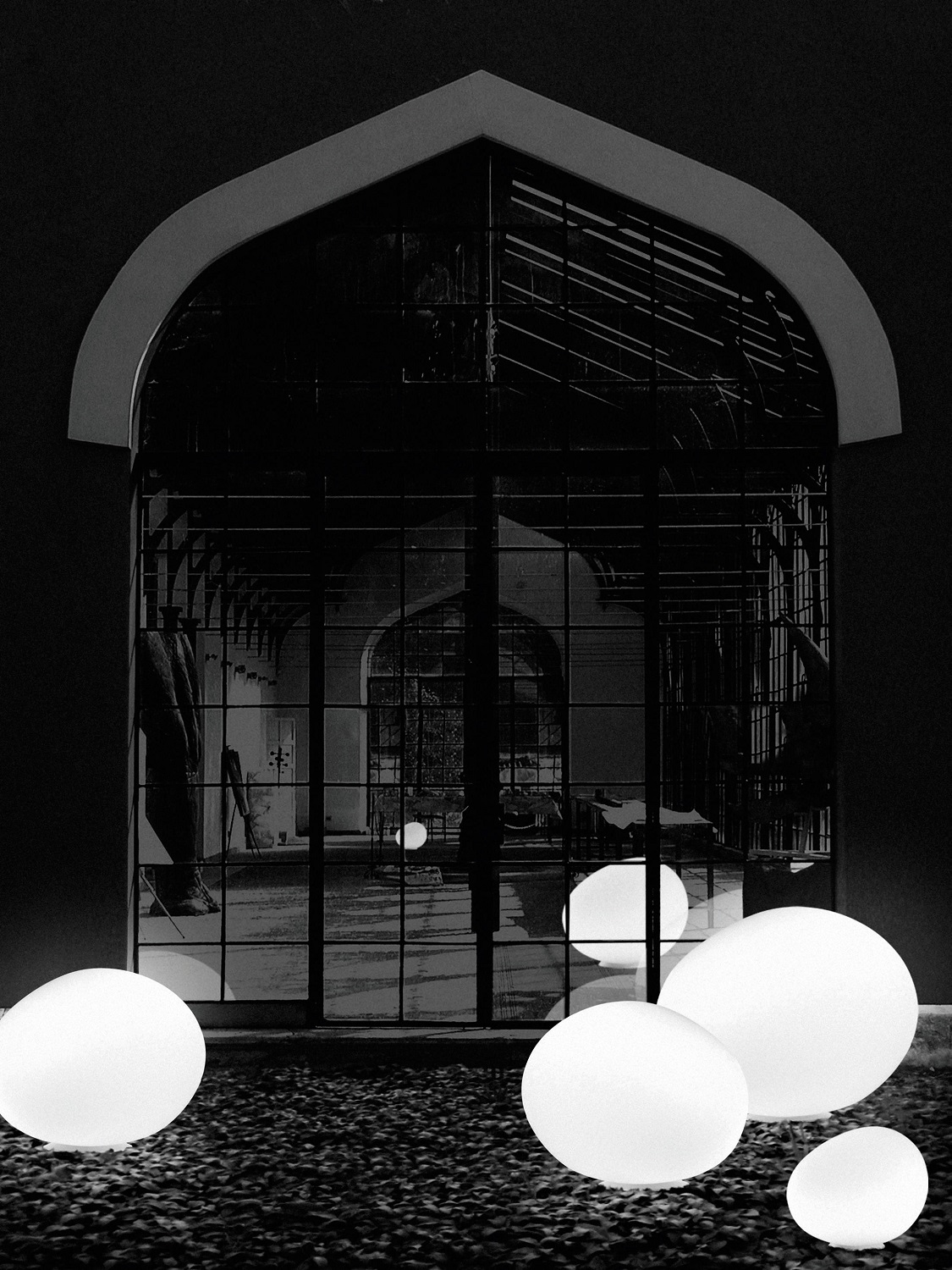 Gregg Outdoor Bodenleuchten von Foscarini, stilvolle Gartenbeleuchtung in Kieselform vor einem Fenster, Schwarz-Weiß.