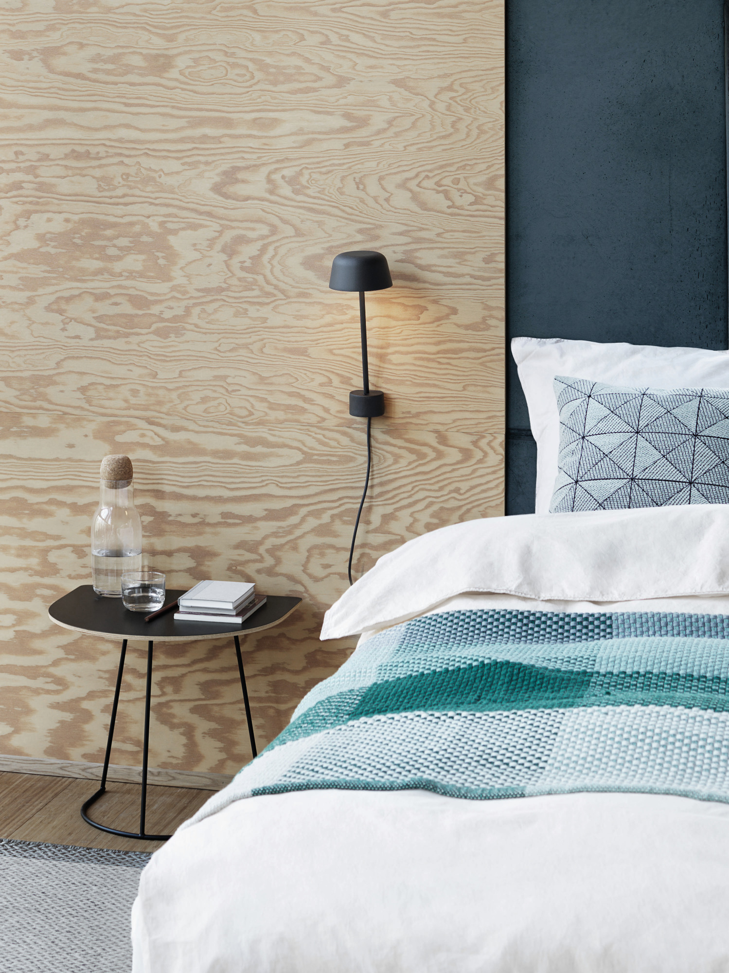 Schwarzer Airy Coffee Table Beistelltisch von Muuto neben einem Bett mit Wasserflasche und Büchern.