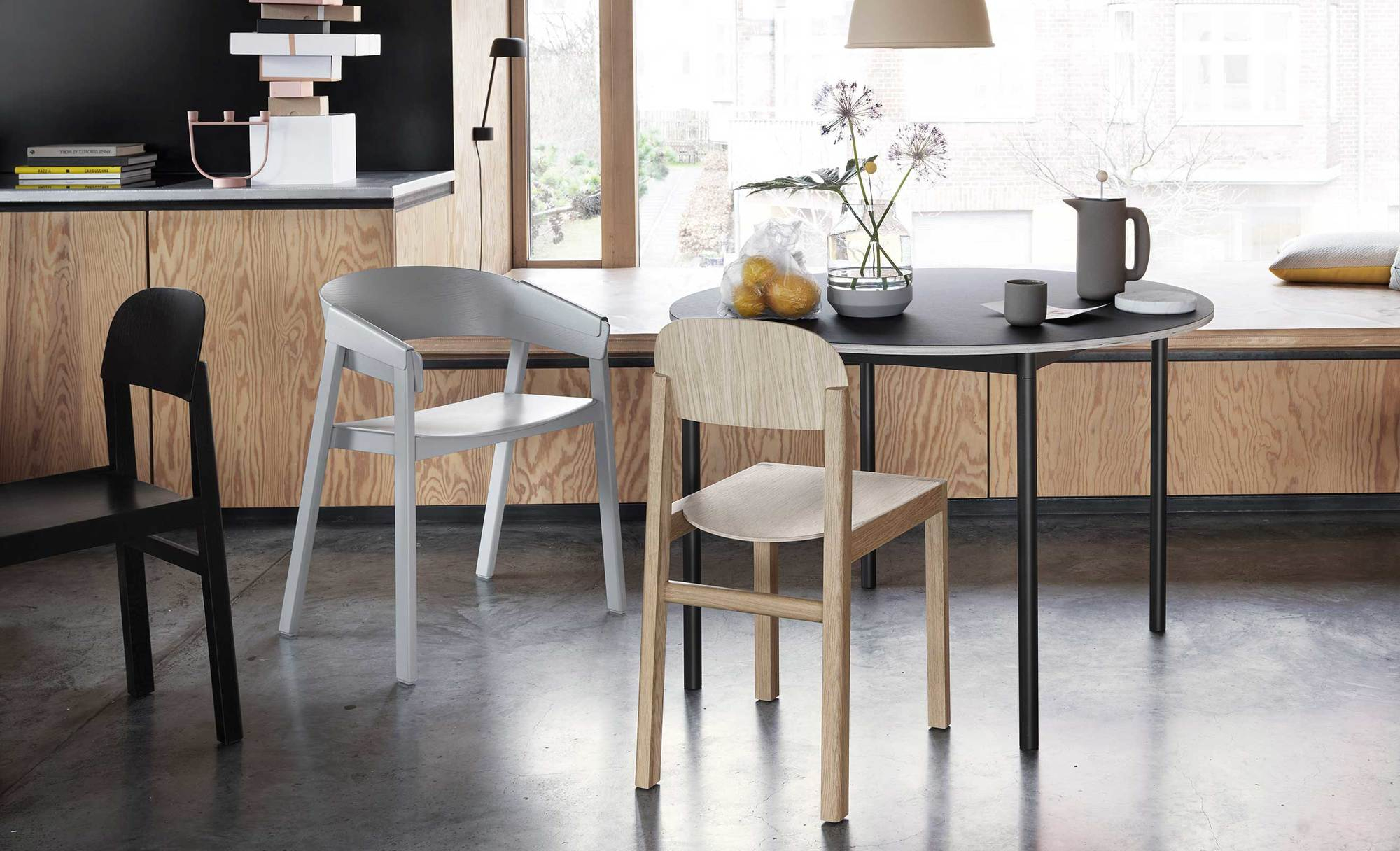 Muuto Base Table Round Tisch mit Stühlen in modernem Esszimmer, schwarze Tischplatte, Holzstühle.