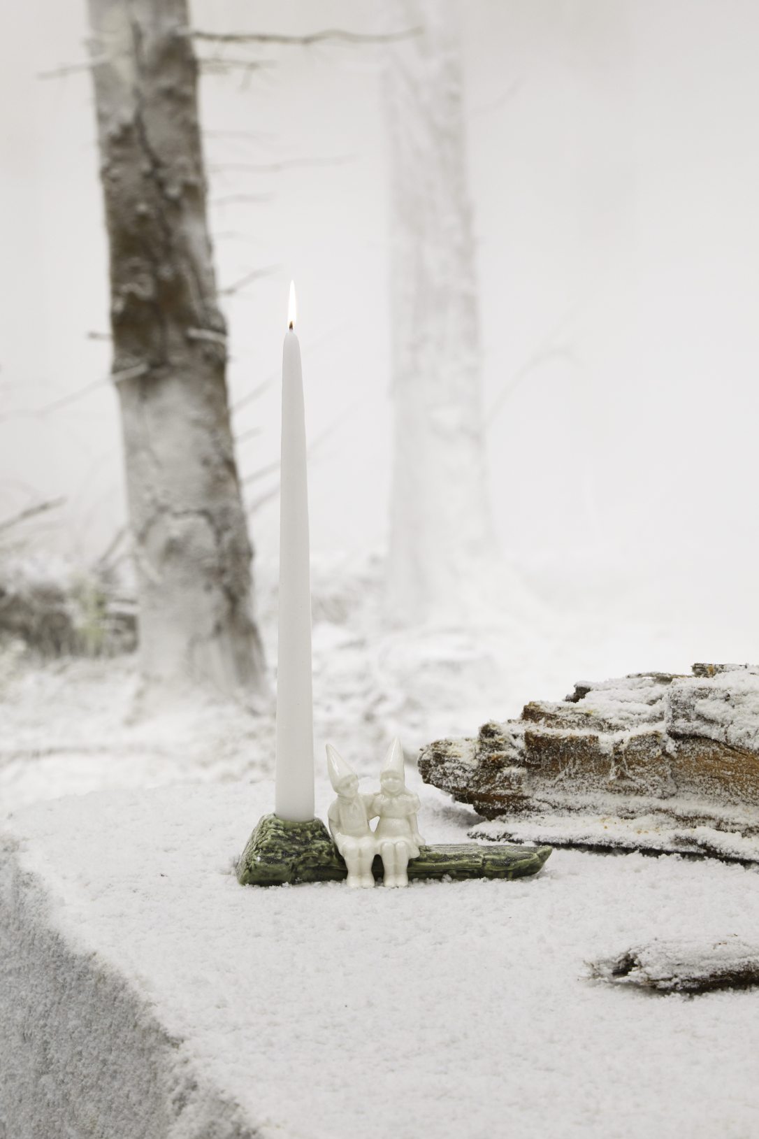 Christmas Tales Julekram Kerzenständer mit brennender, weißer Kerze und zwei kleinen Figuren im winterlichen Schnee.