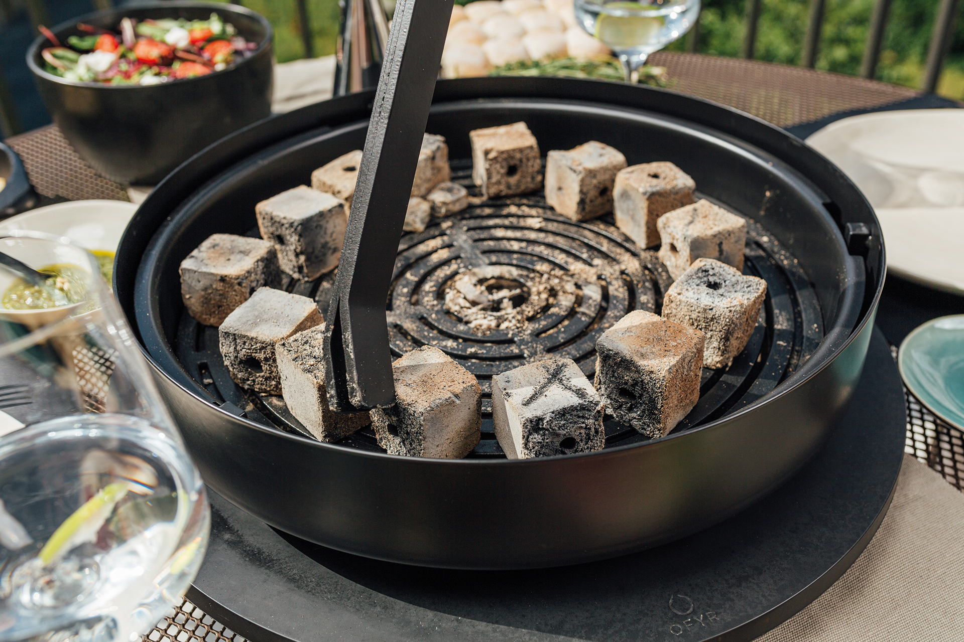 Tabl'O Tischgrill von Ofyr mit Briketts und Grillzange für ein gemütliches Barbecue im Freien.