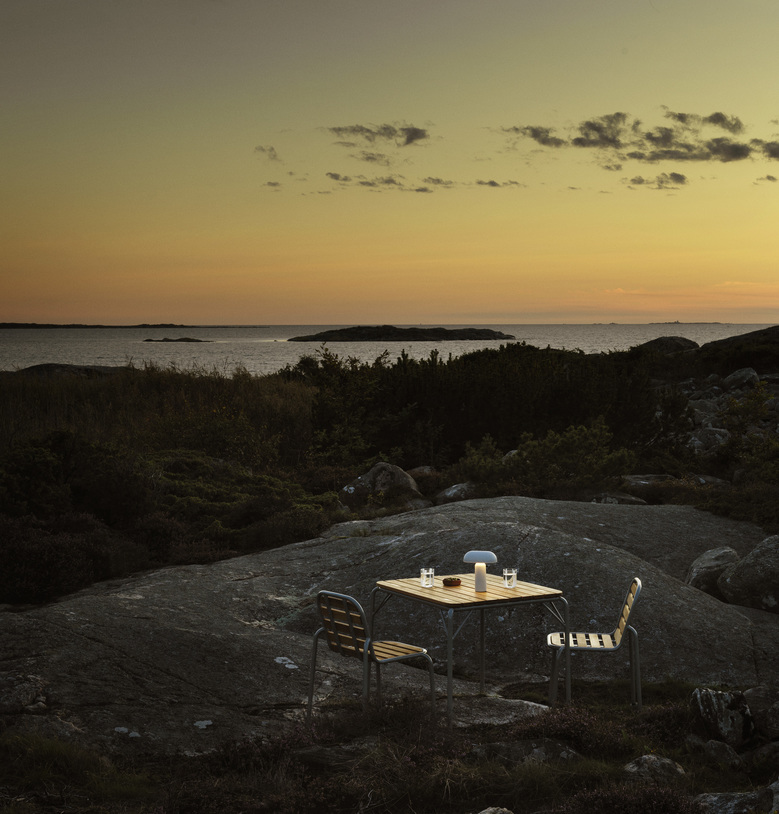 Normann Copenhagen Vig Table 90x90 cm Outdoor Tisch mit zwei Stühlen auf Felsen am Meer.