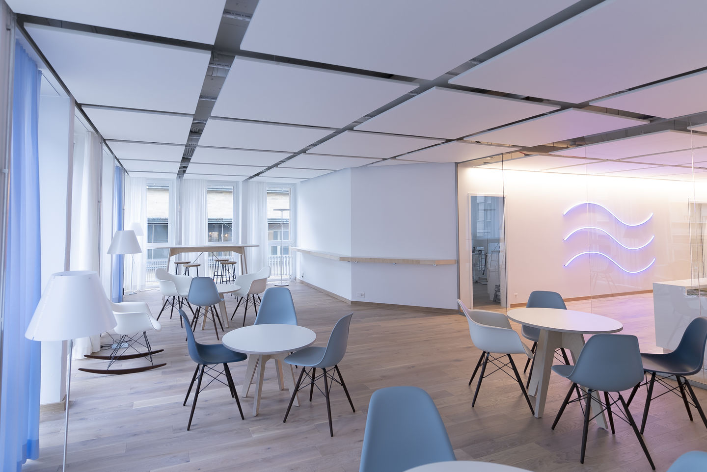 Heller Raum mit mehreren Eames DSW Stühlen von Vitra in Weiß und Blau um Tische gruppiert.