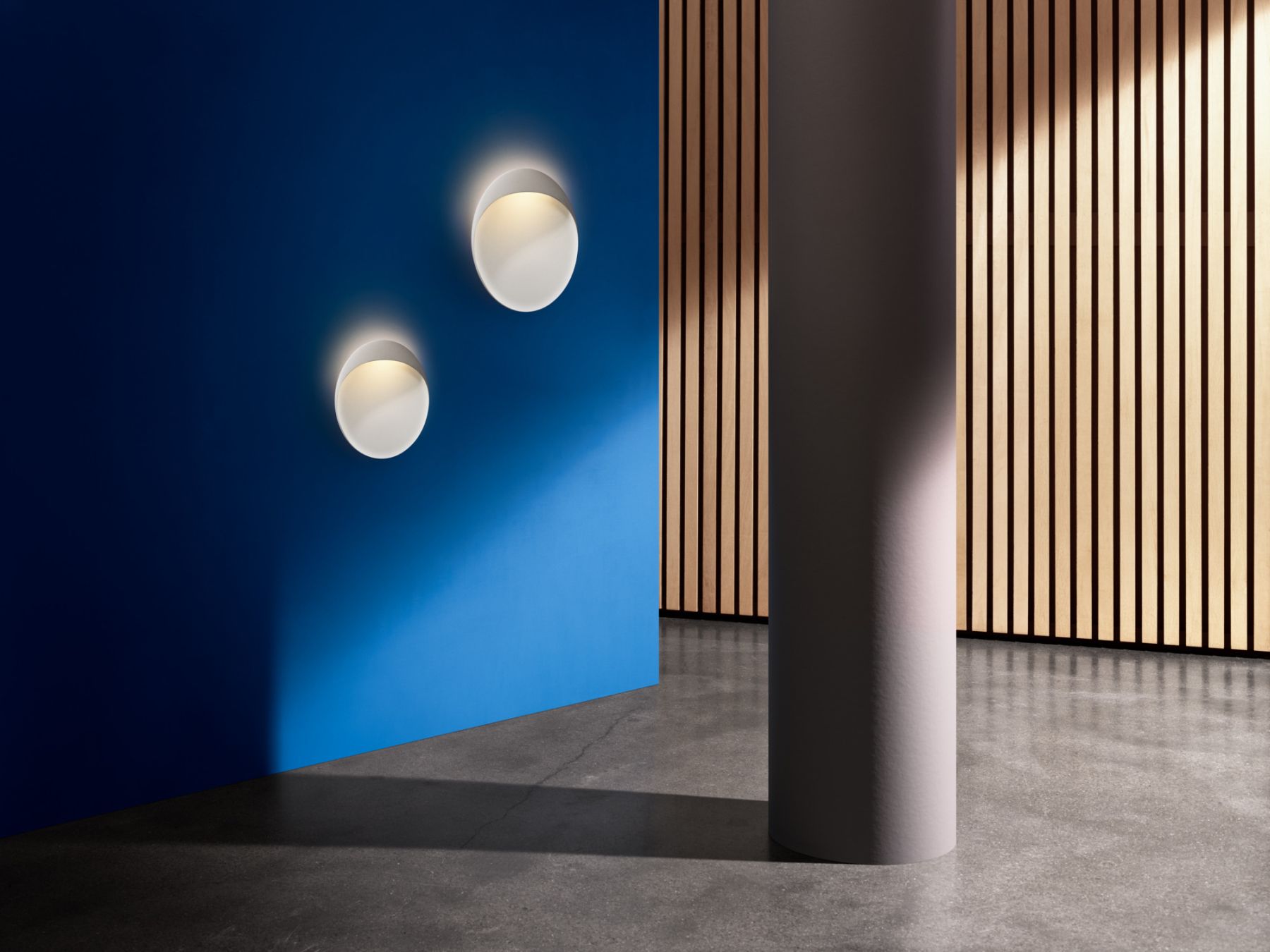 Zwei runde, weiße Flindt Wandleuchten von Louis Poulsen an einer blauen Wand, indirekte Beleuchtung.