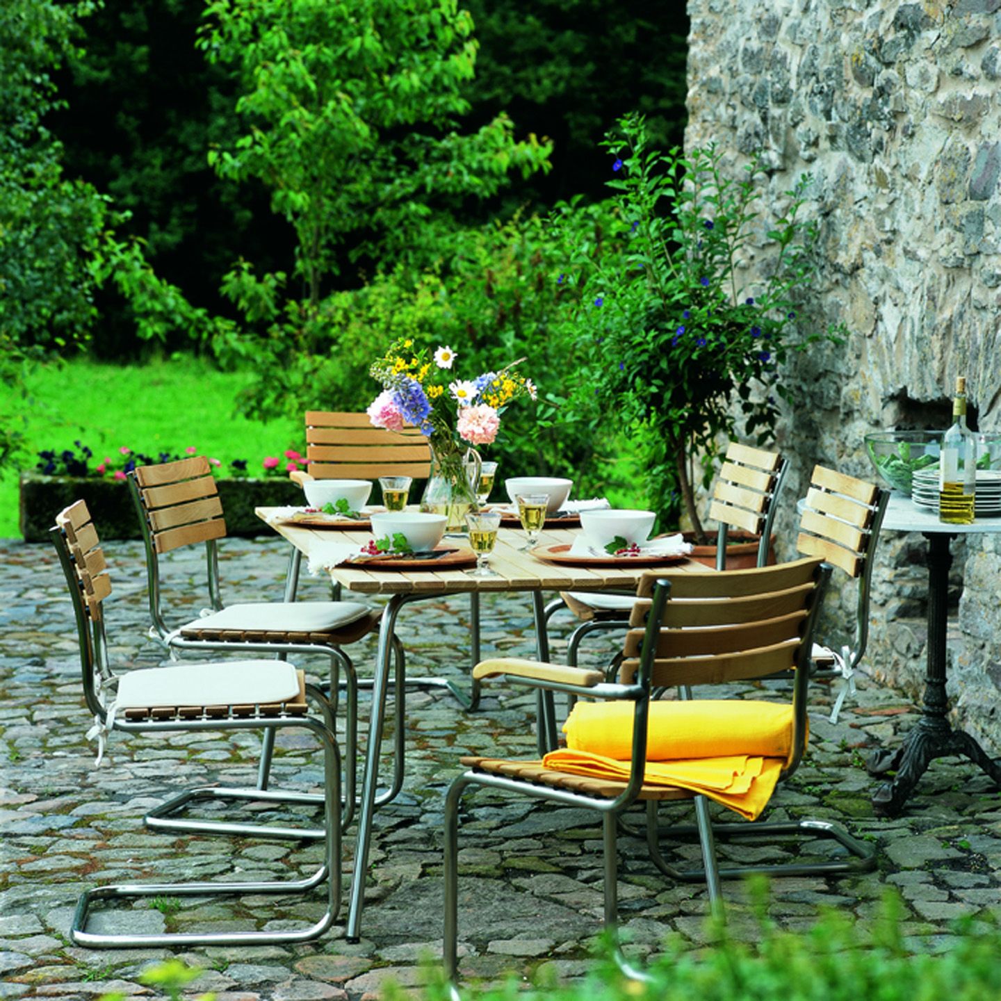 Gartenszene mit Thonet S 40 Freischwinger Stühlen aus Holz und Stahl um einen Esstisch.