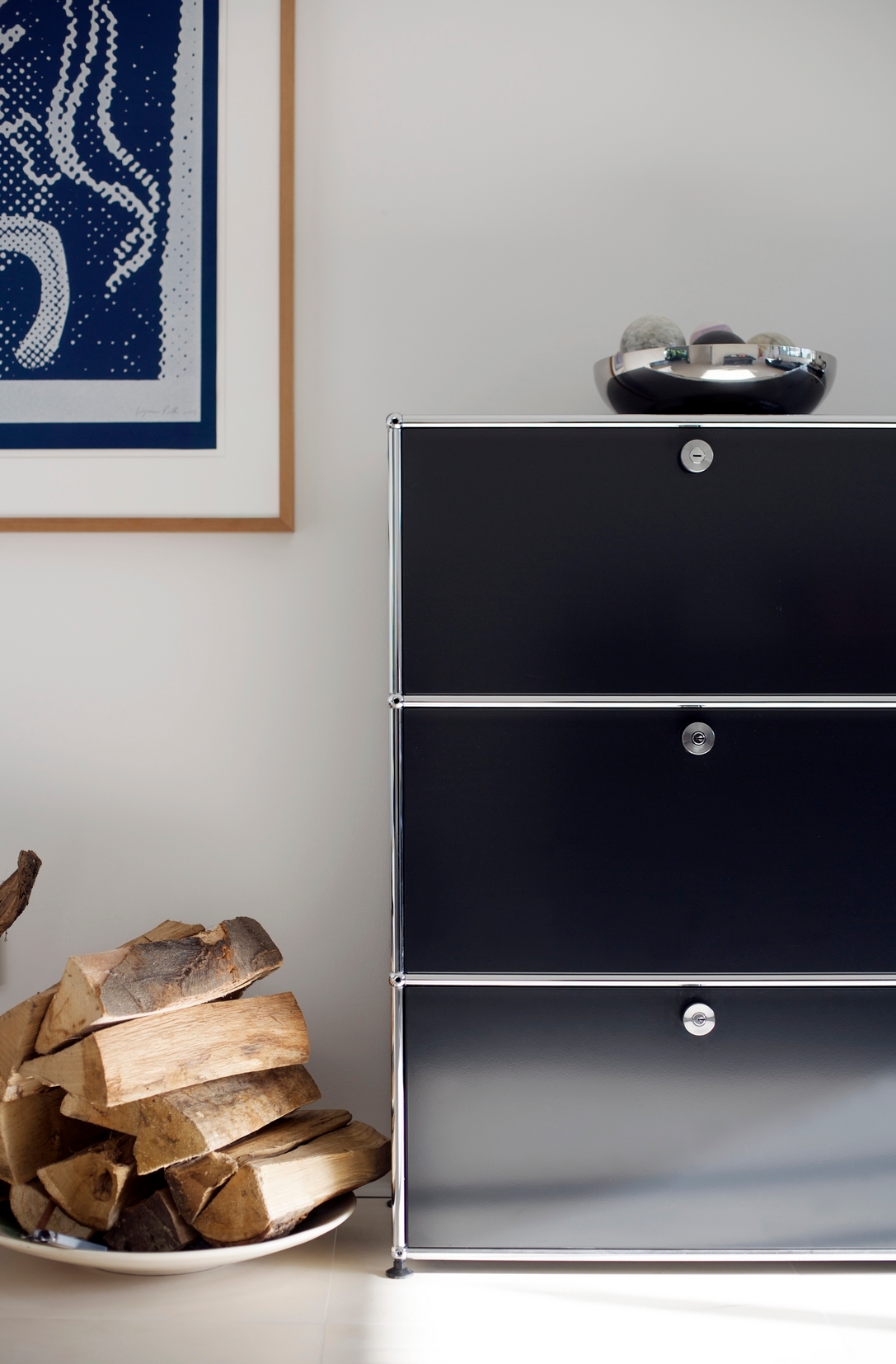 Schwarzes USM Haller Highboard mit drei Klappen, Chromgestell und Deko-Elementen im Wohnzimmer.