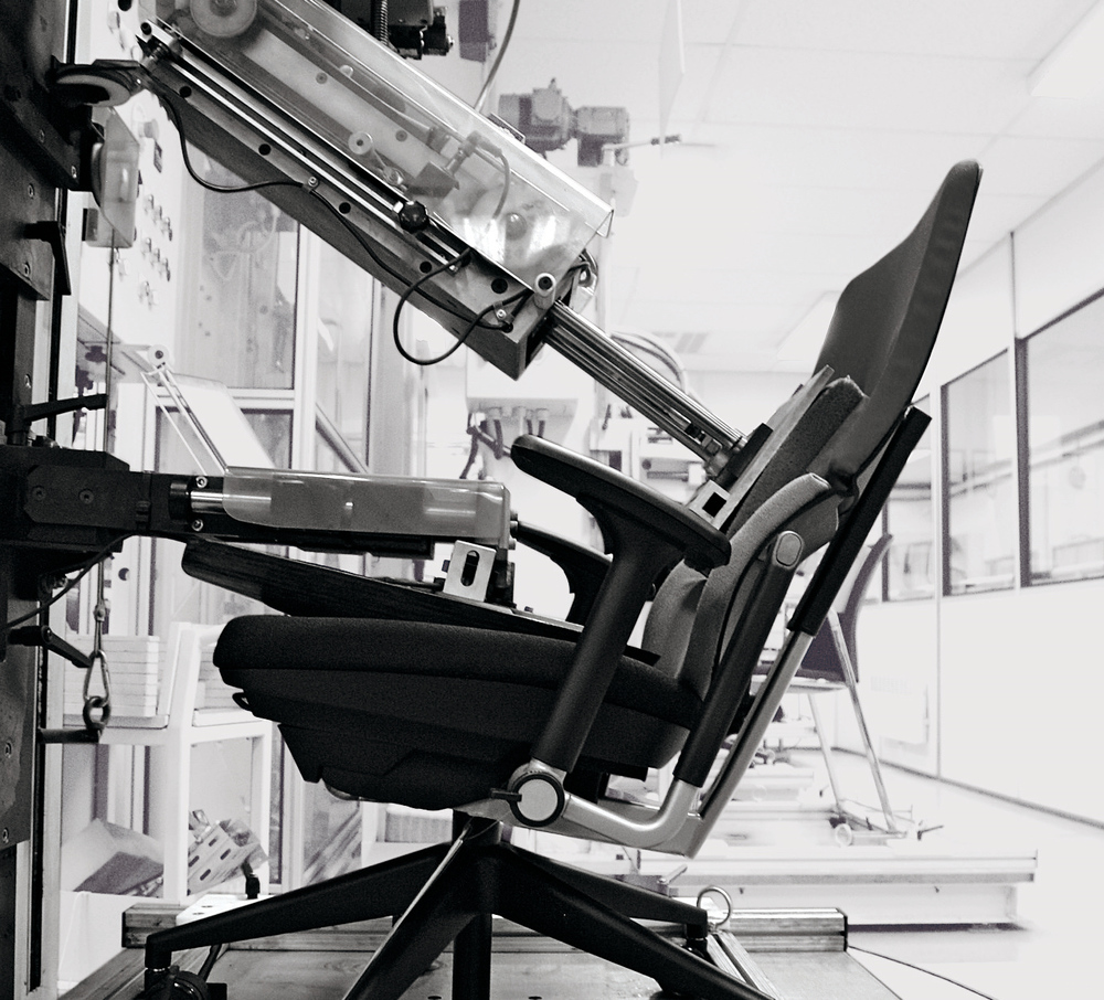 Schwarz-Weiß-Foto eines Please Drehstuhls von Steelcase im Testlabor, geprüft mit einer Maschine.
