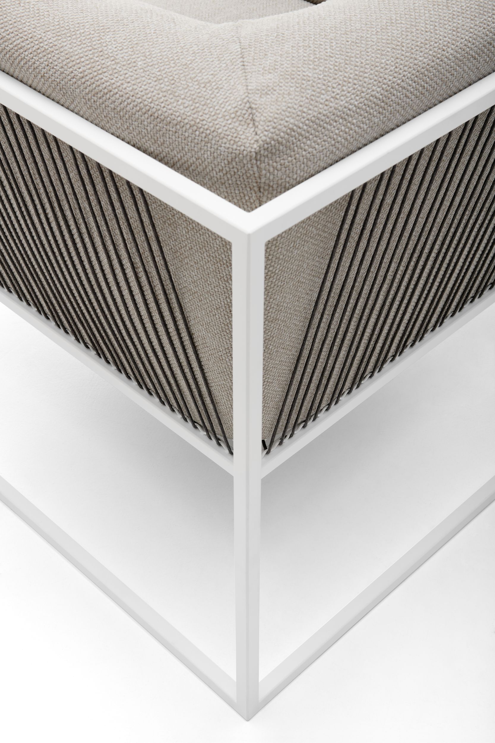 Detailaufnahme des Arpa Sessels: Weißes Gestell, beiger Stoffbezug und dunkle Seilbespannung.