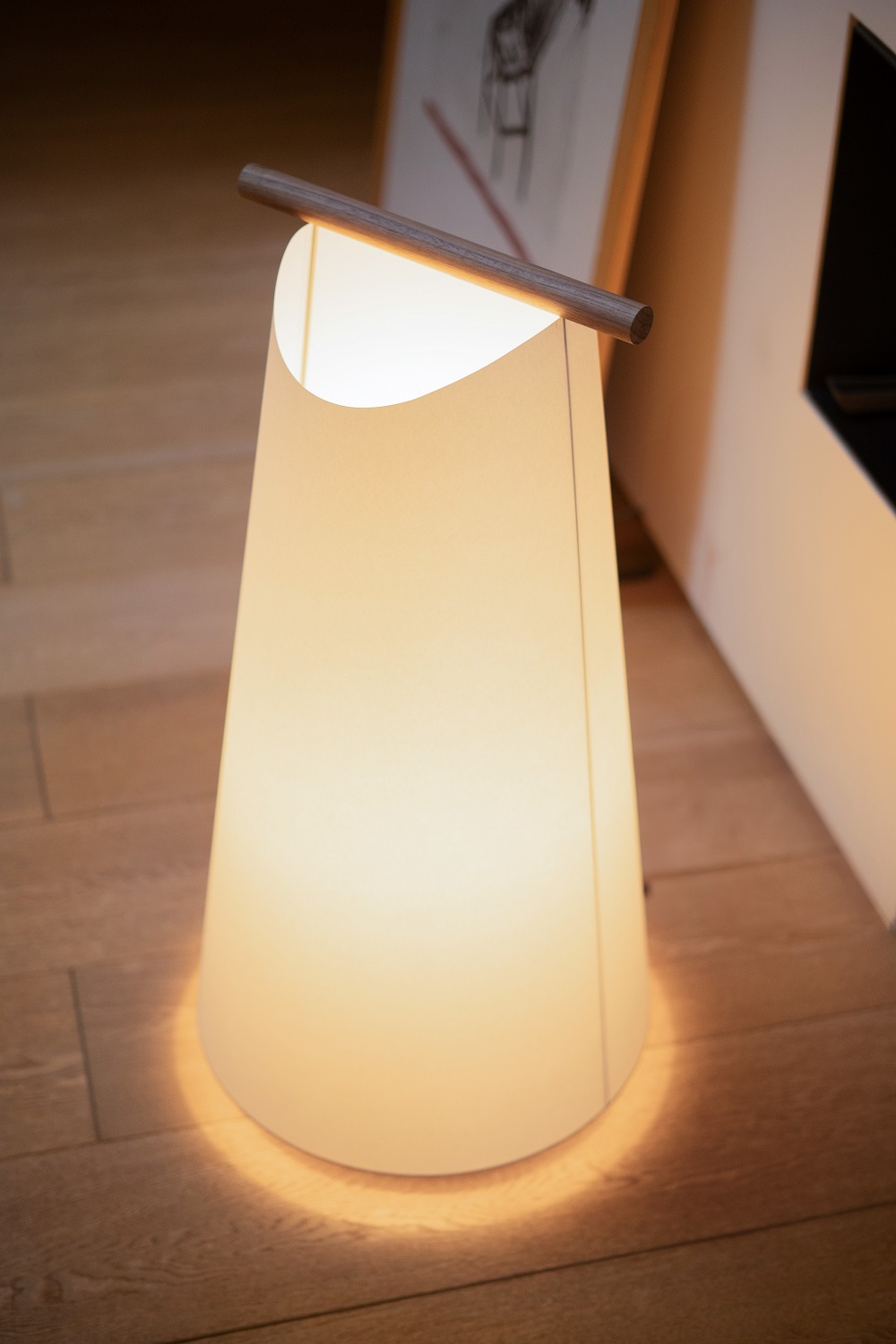 Nomon Catay Stehleuchte: Kegelförmige Designerlampe mit Holzdetail und warmem Lichtschein auf Holzboden.