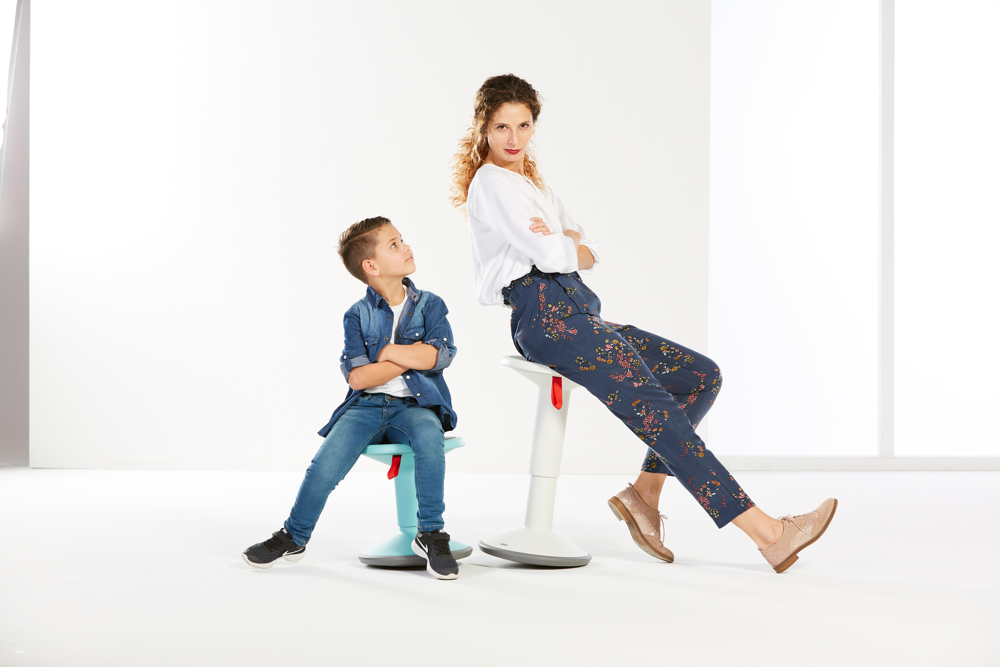 Interstuhl UP Junior Edition: Kind sitzt auf lachsorangem Kinderhocker, Frau lehnt an weißem Stehhocker.