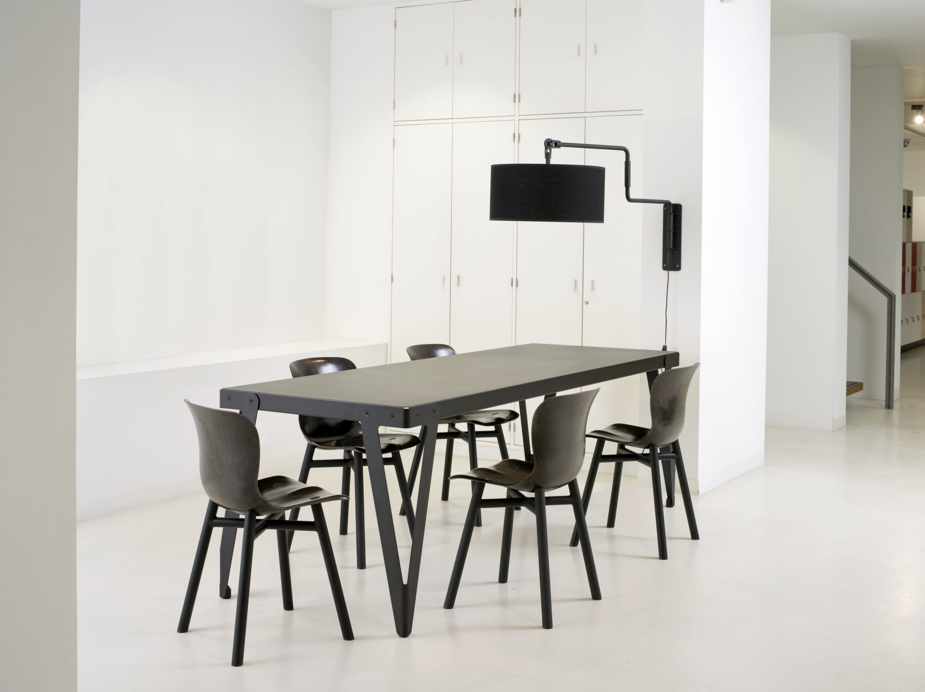 Schwarzer Lloyd Indoor Table Tisch Functionals mit passenden Stühlen und Lampe in minimalistischem, weißem Raum.