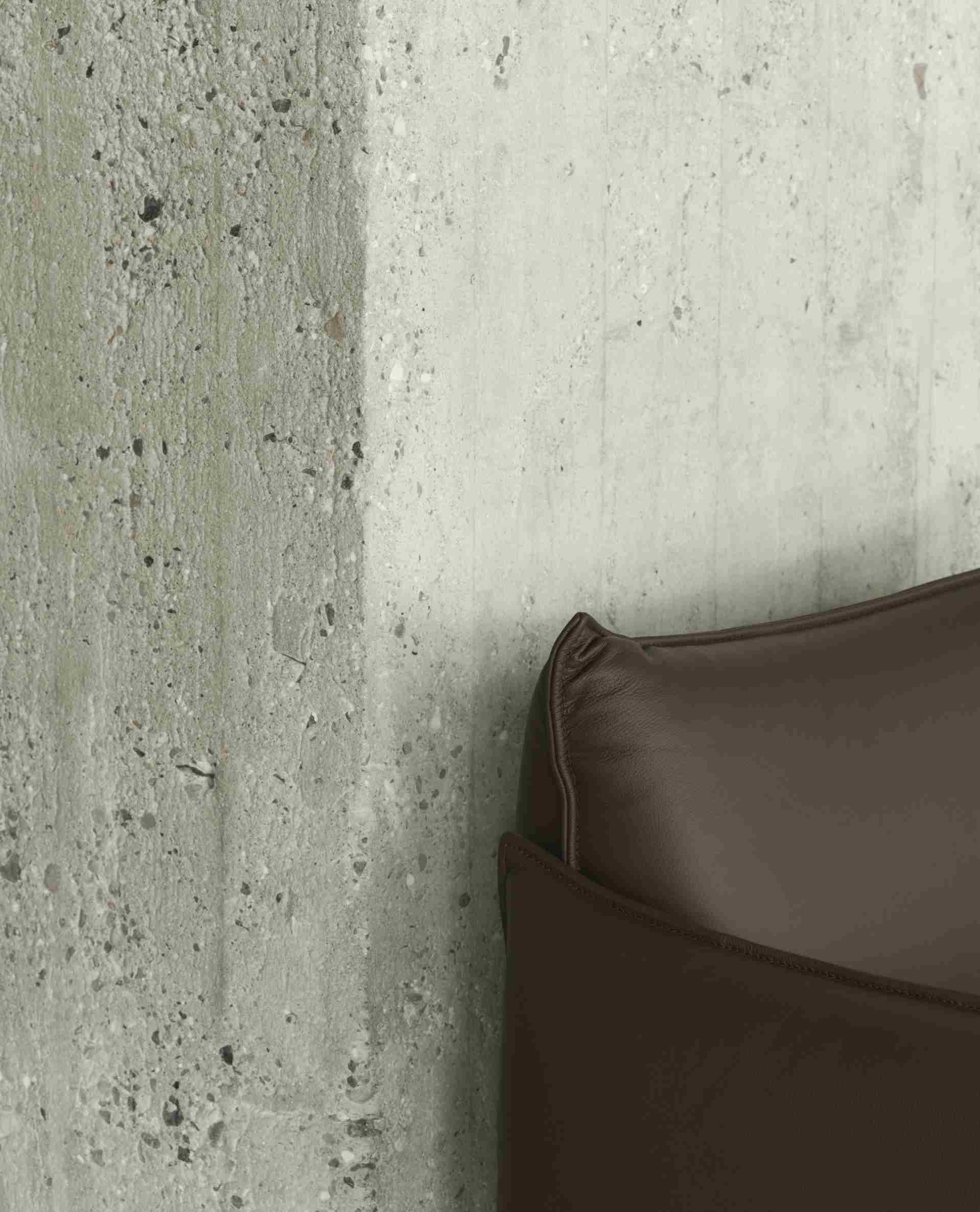 Detailaufnahme des braunen Ark Lounge Sessels von Normann Copenhagen vor einer grauen Betonwand.