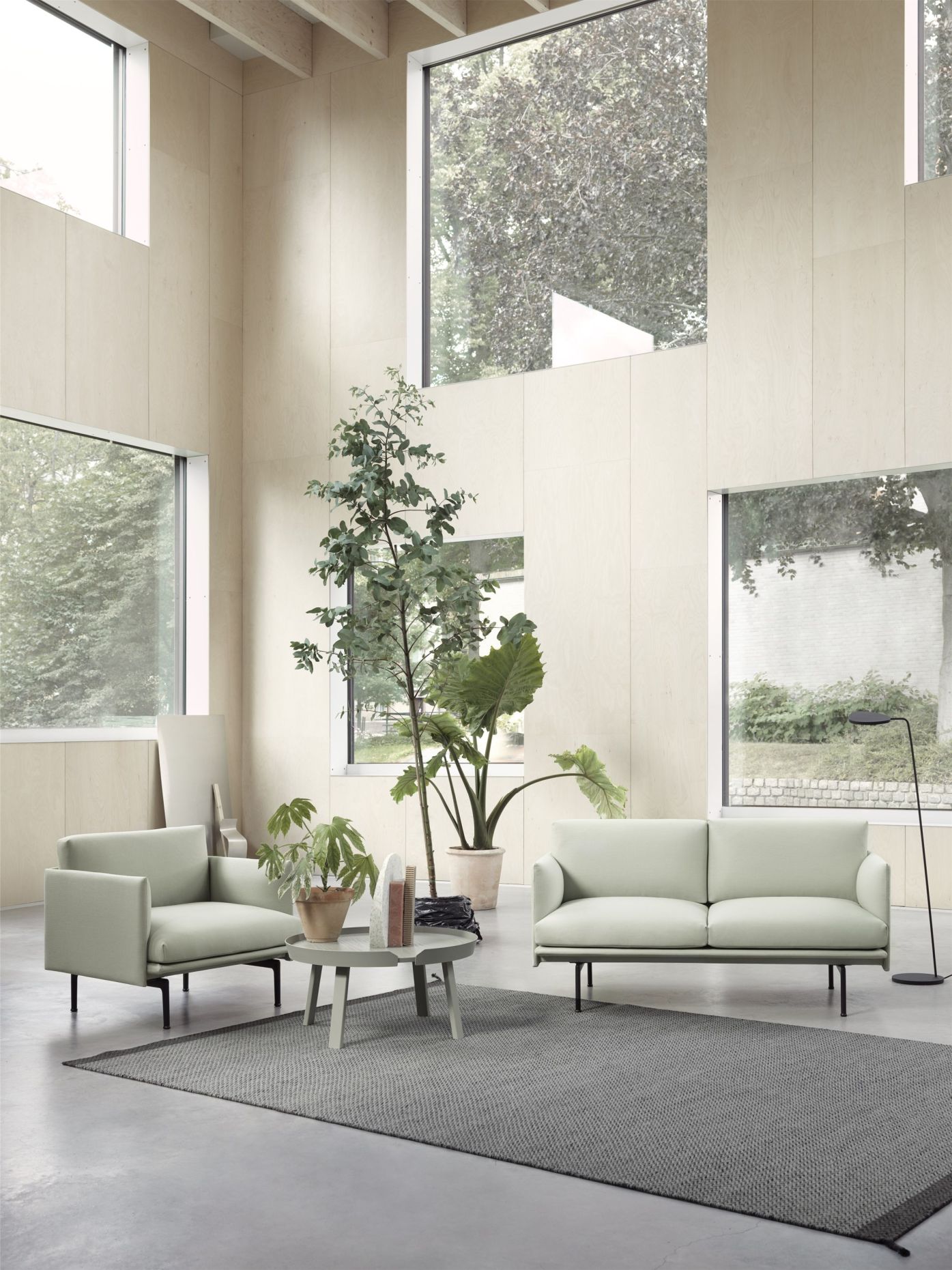 Helles Wohnzimmer mit mintgrünem Sofa, Sessel und grauem Teppich. Moderne Möbel und Zimmerpflanzen.