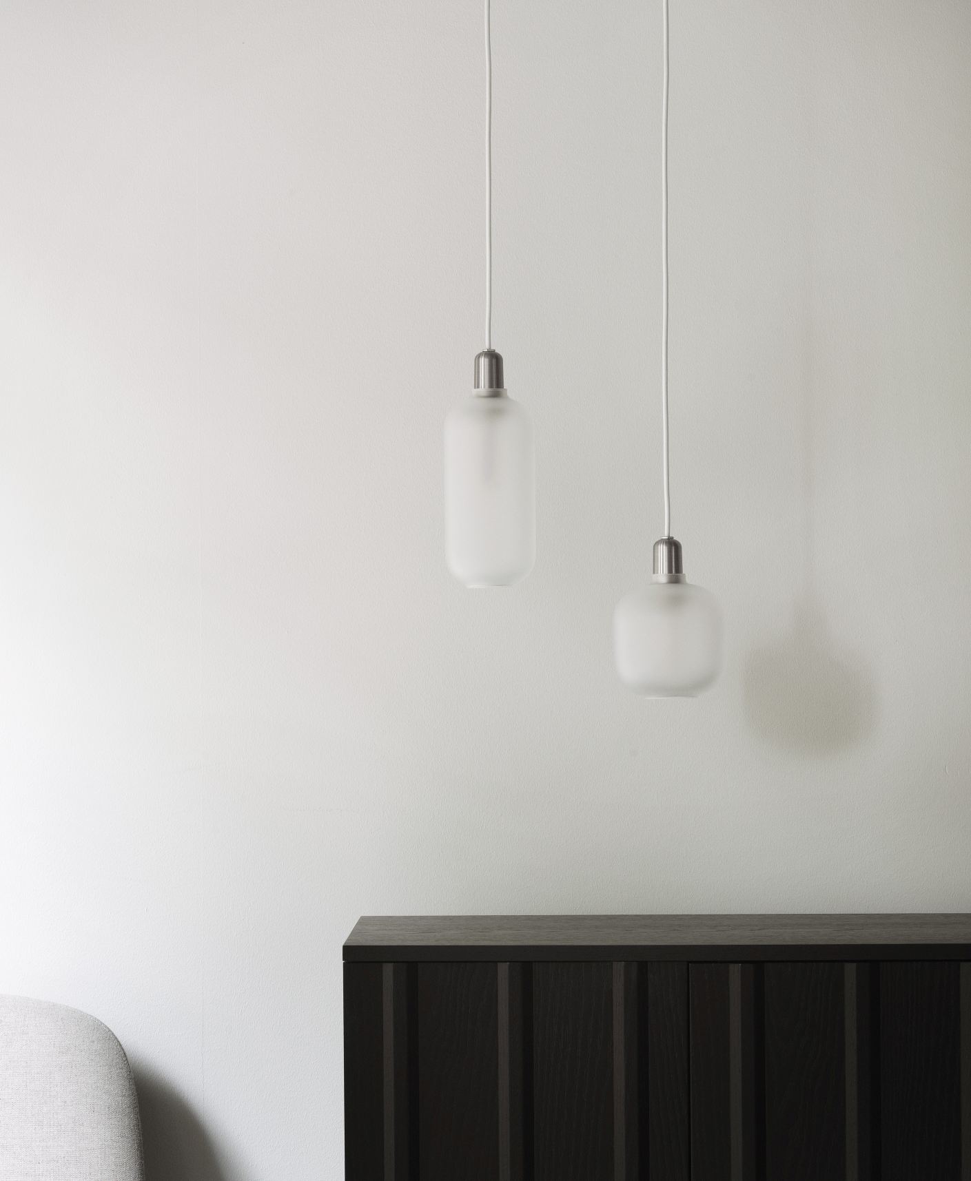 Dunkles Rib Sideboard von Normann Copenhagen unter zwei modernen, matt-weißen Pendelleuchten vor einer weißen Wand.