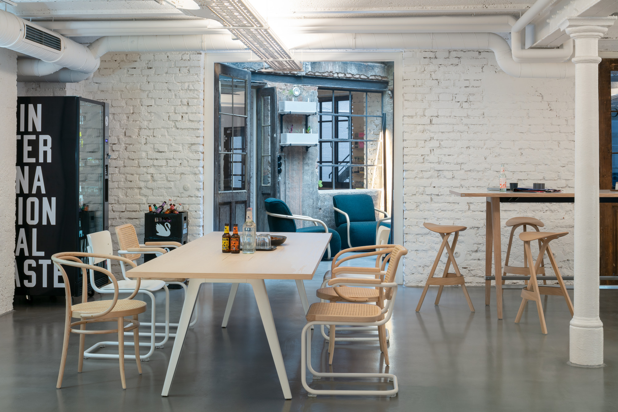 Heller Raum mit Thonet 1500 Tisch, Stühlen und Barhockern aus Holz und Wiener Geflecht.