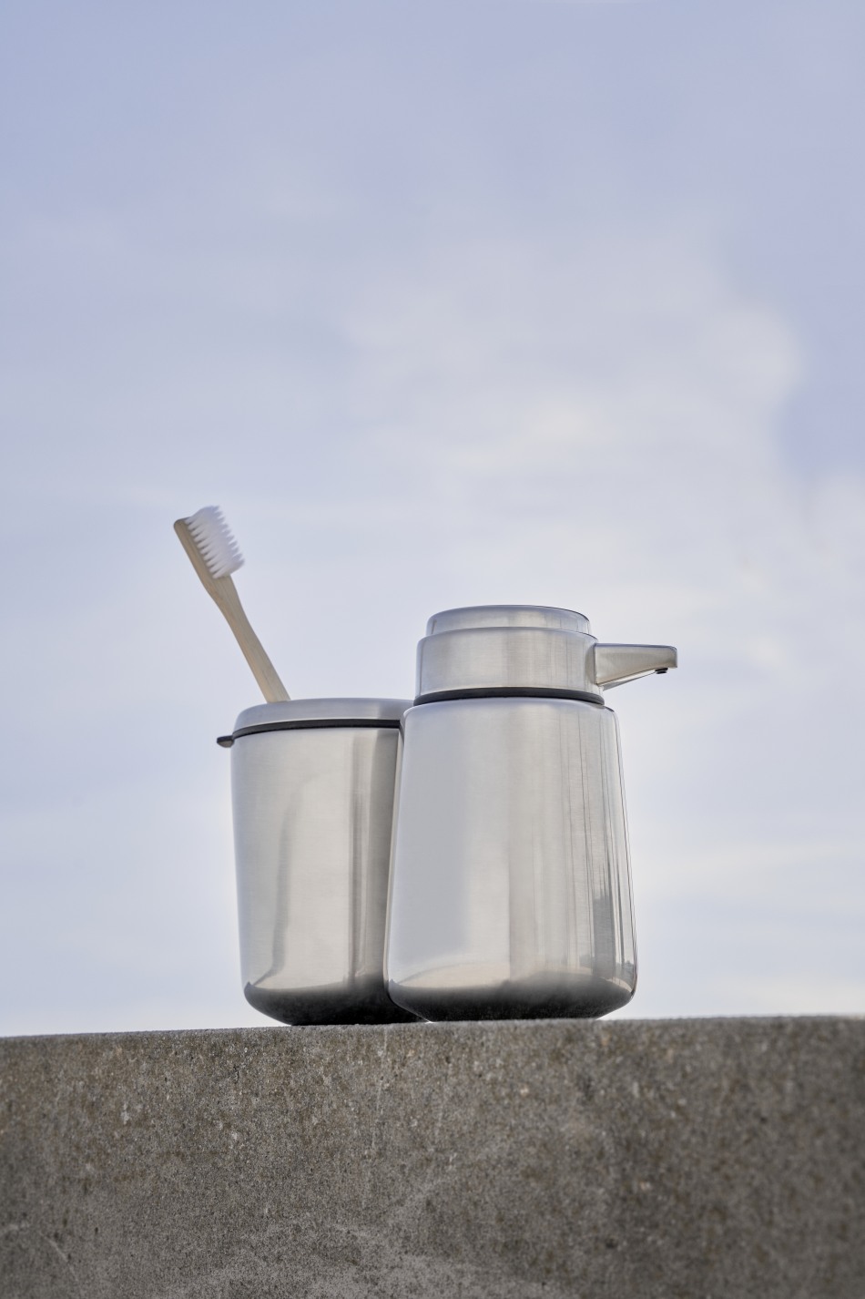 Vipp Zahnbürstenhalter aus Edelstahl mit Zahnbürste und Seifenspender vor hellem Himmel. Badaccessoires für moderne Badezimmer.