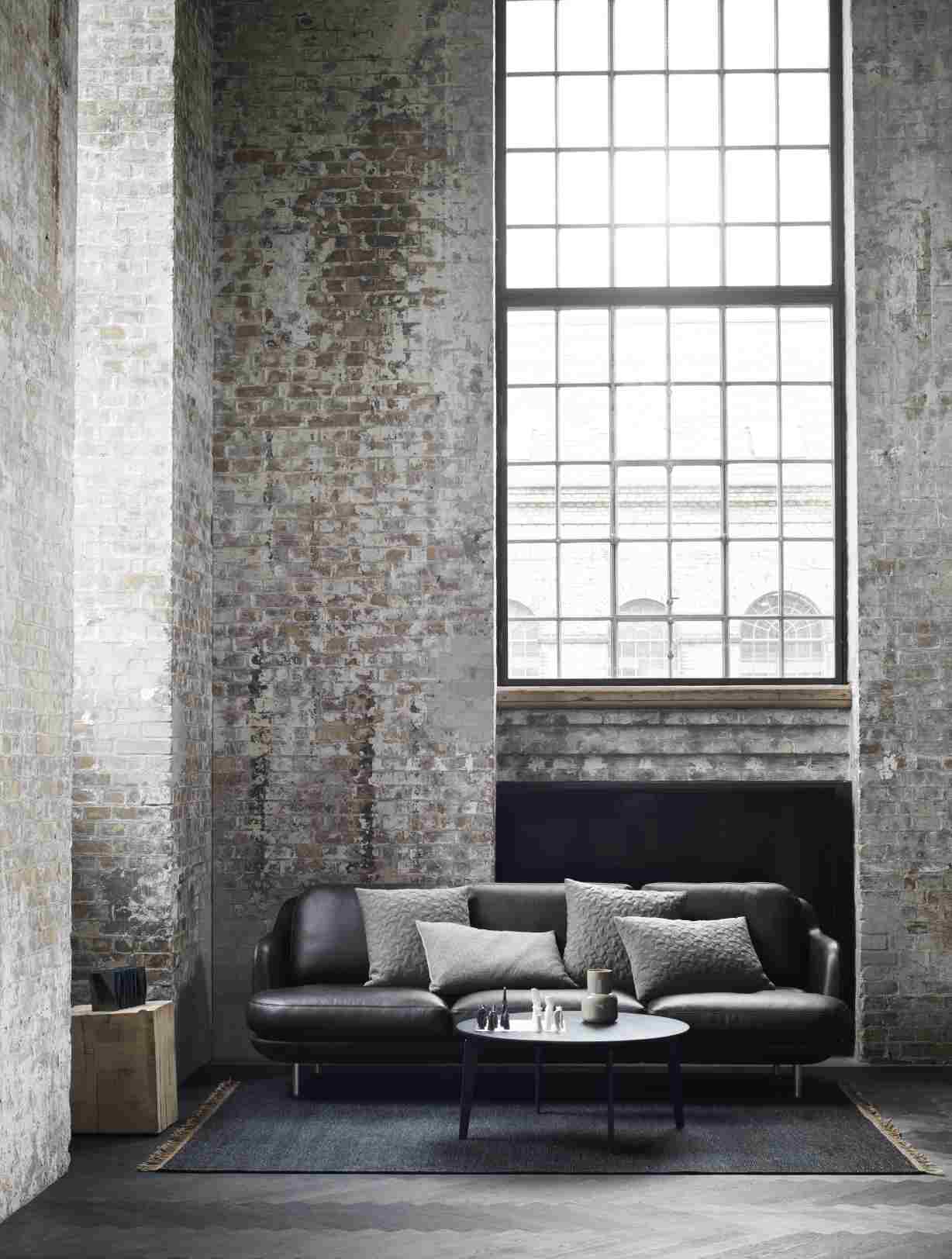 Schwarzes Fritz Hansen Lune Sofa mit grauen Kissen in einem Loft mit Backsteinwand und großem Fenster.