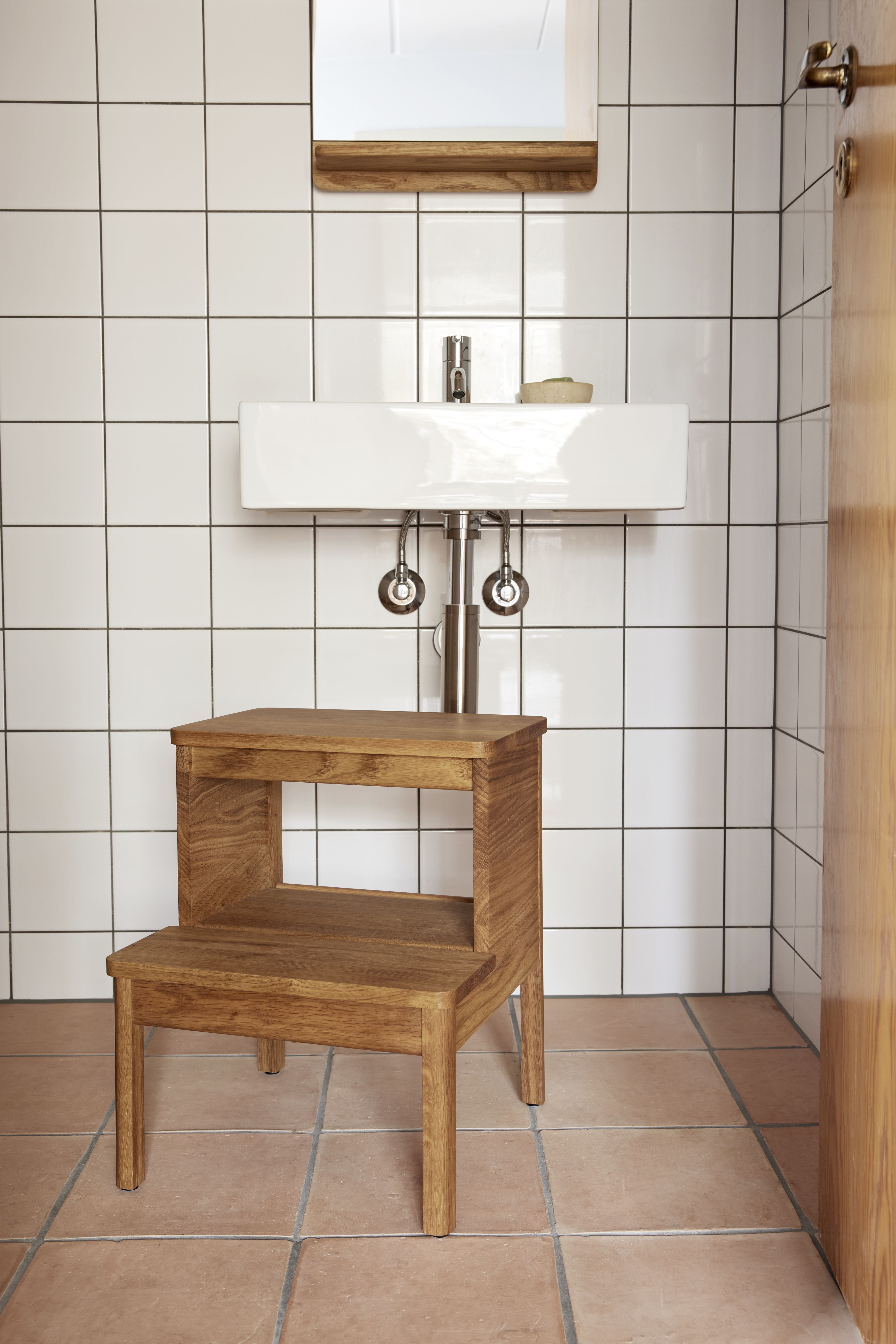 A Line Steighocker von Form & Refine aus Eichenholz im Badezimmer vor einem Waschbecken.