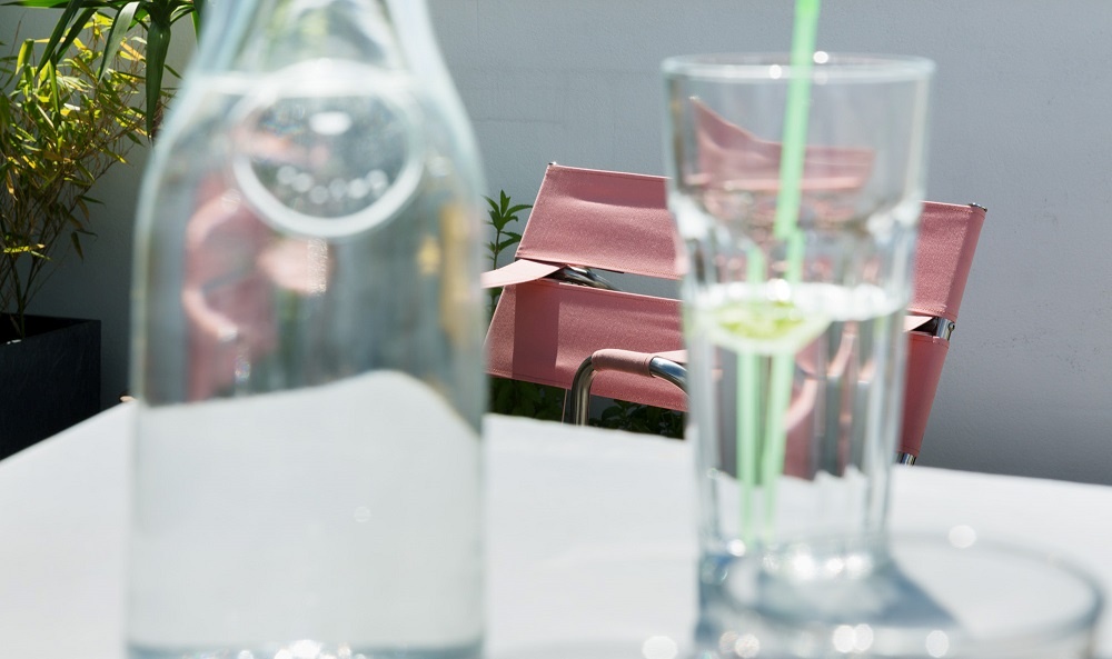 Nahaufnahme: Tecta D4 Bauhaus Faltsessel in Rosa, gesehen durch Wasserflasche und Glas mit Strohhalm.