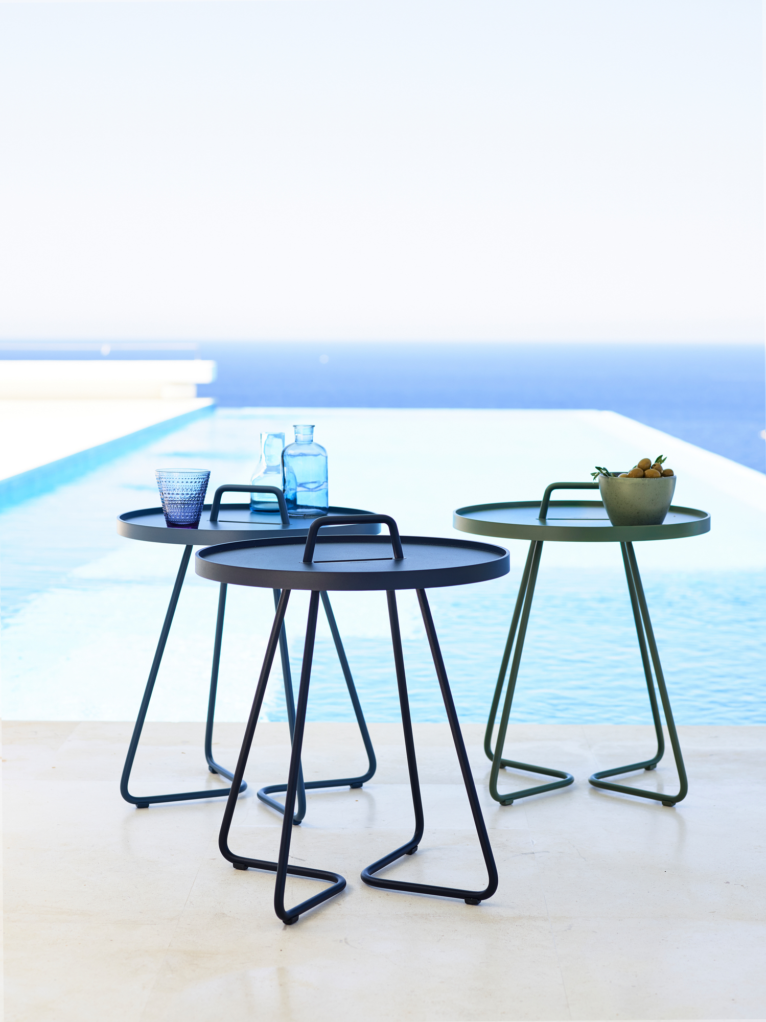 Drei Cane-Line On-The-Move Outdoor Beistelltische in Schwarz und Grün vor einem Pool.