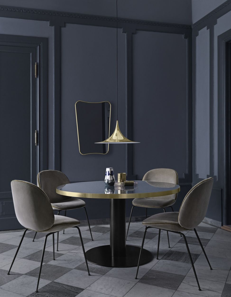 Esszimmer mit Gubi F.A. 33 Wandspiegel, rundem Tisch, Pendelleuchte und vier Stühlen in dunklem Ambiente.