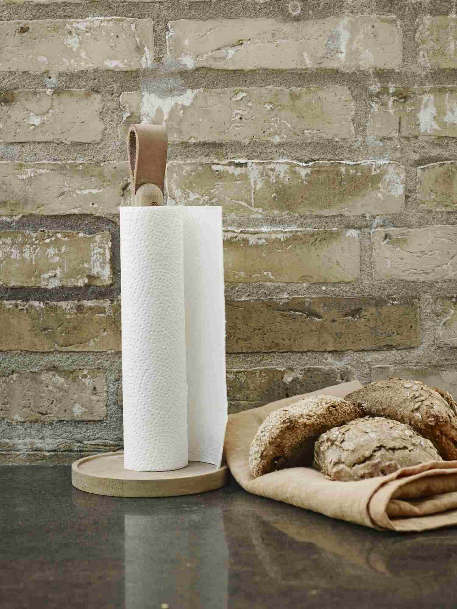 Norr Küchenrollenhalter aus Holz mit Papierrolle und Ledergriff vor Backsteinmauer.