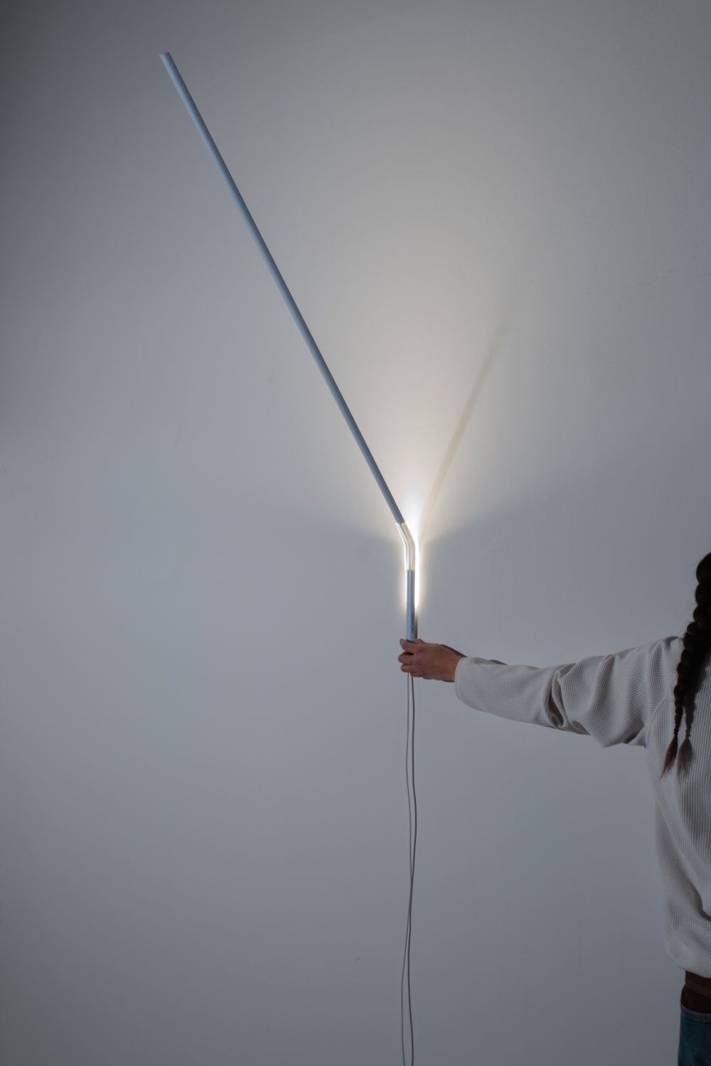 Weiße Measure Light Wandleuchte von Ingo Maurer an einer Wand, gehalten von einer Person.
