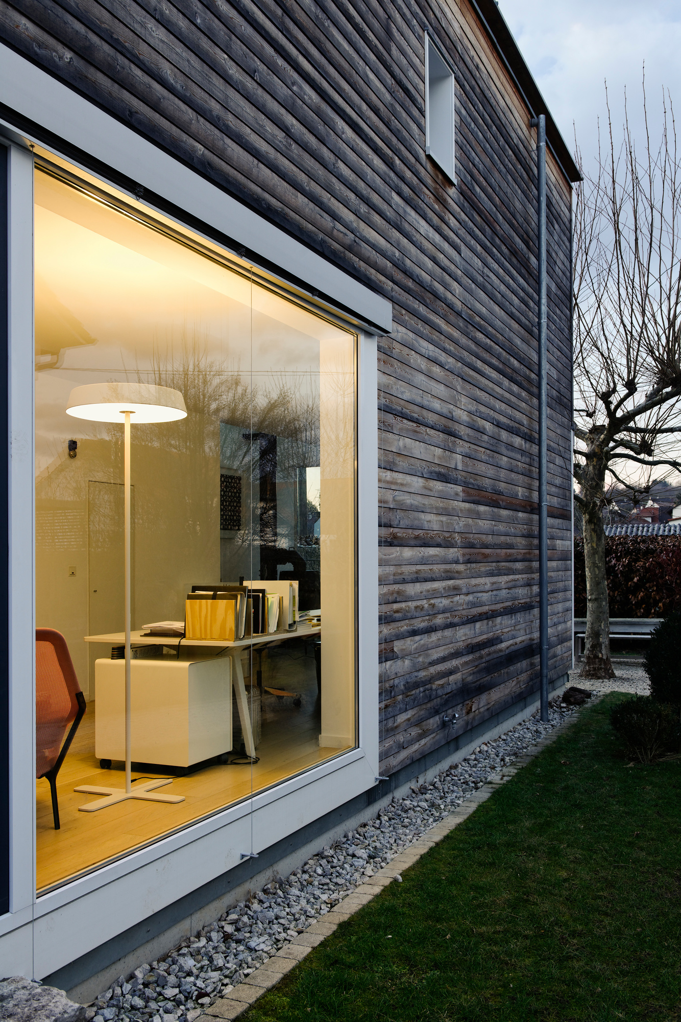 Koi S LED Stehleuchte von Belux, gesehen durch ein Fenster, beleuchtet einen modernen Arbeitsbereich.