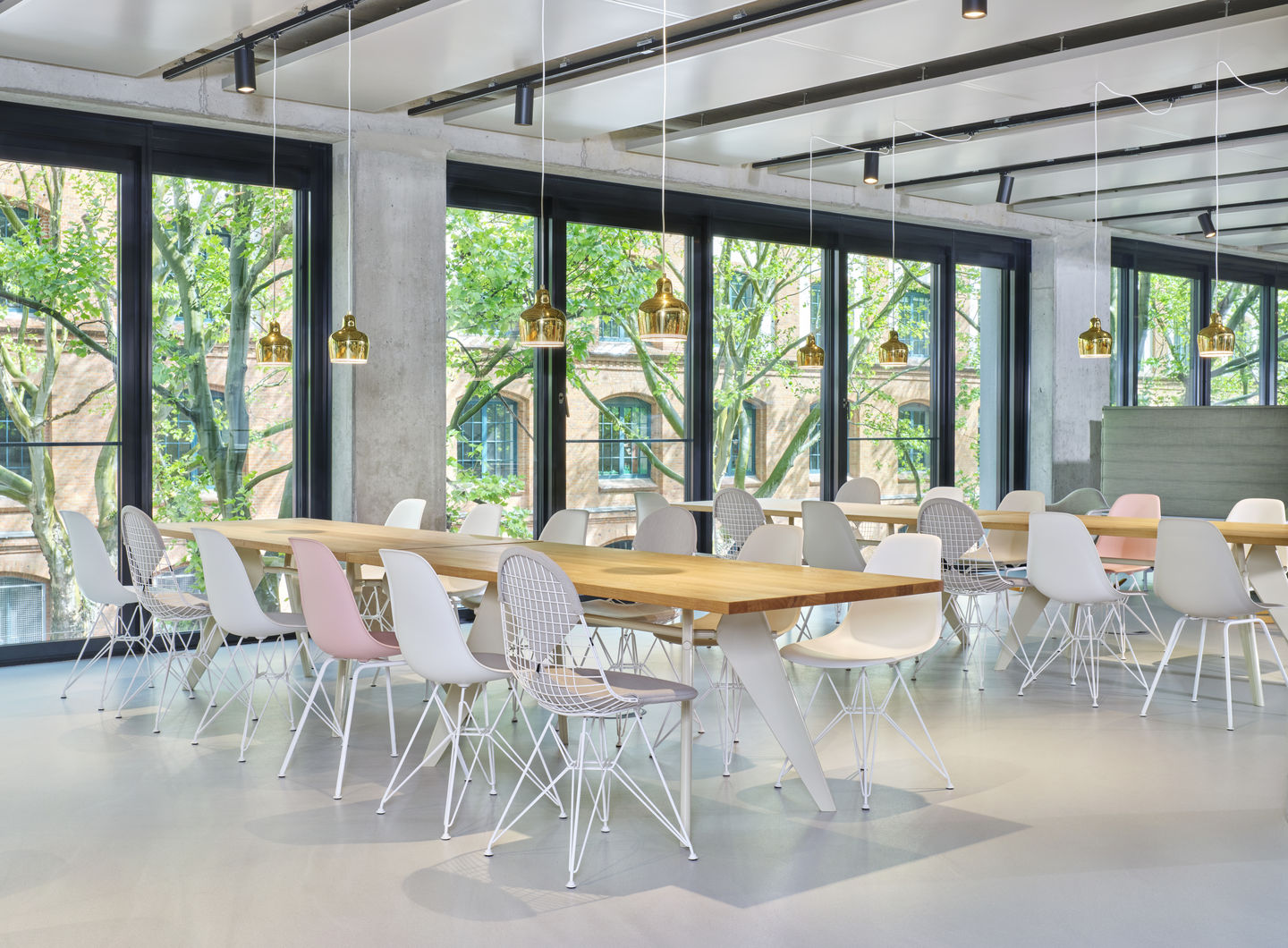 Helle Büroraum-Szene mit langen Holztischen und mehreren Eames Fiberglass Stühlen DSX mit Sitzpolster von Vitra.