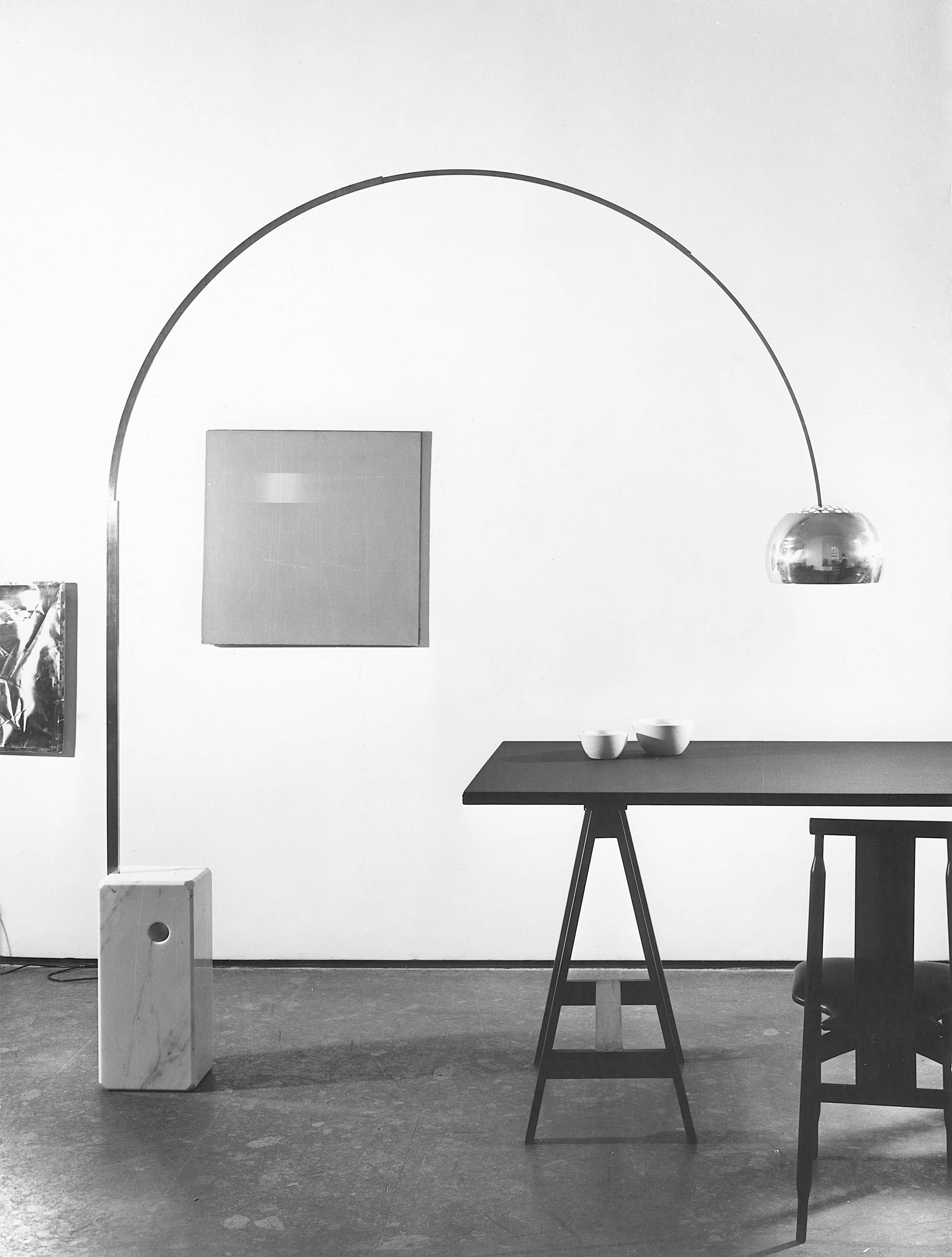 Schwarz-Weiß-Foto einer Bogenlampe mit Chromschirm über einem Tisch mit zwei Schalen.