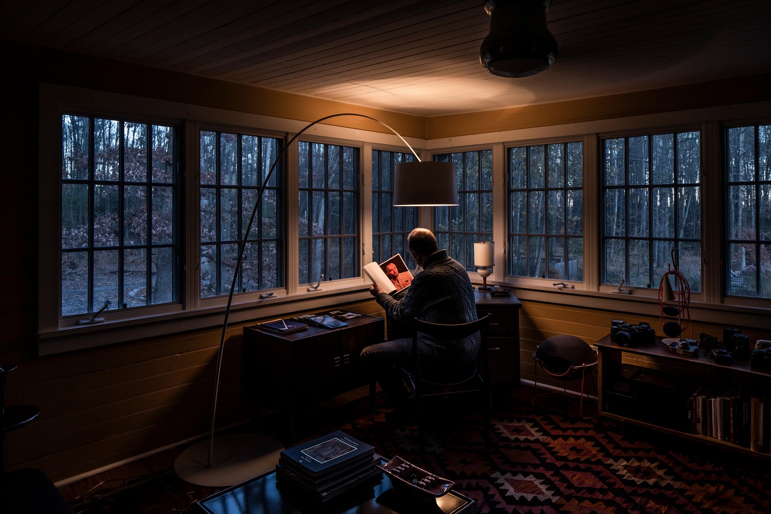 Mann liest unter der Twiggy Stehleuchte von Foscarini in einem gemütlichen, rustikalen Arbeitszimmer mit Blick auf den Wald.