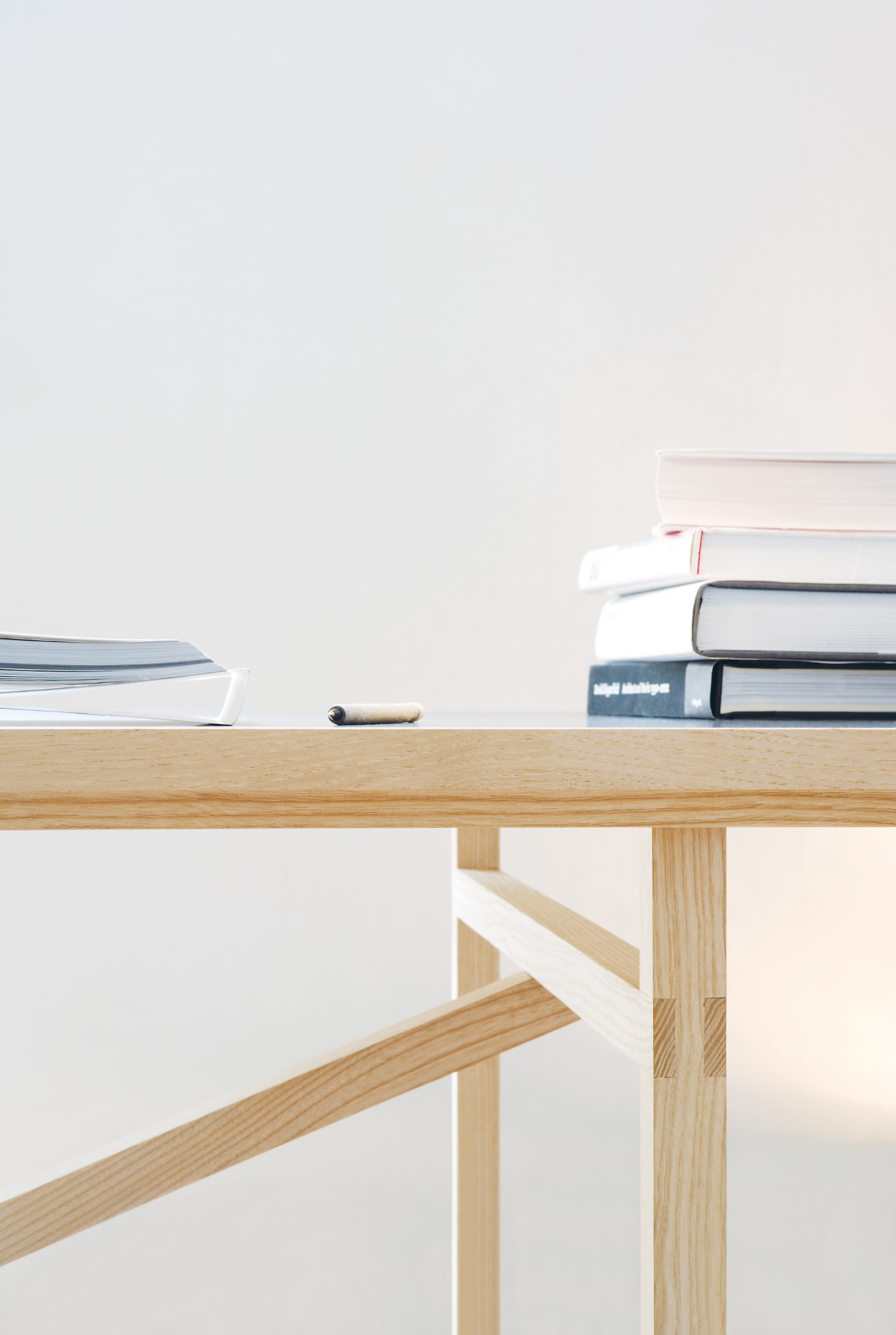 Detailaufnahme vom hellen Holzgestell des Egon Tisch von Nils Holger Moormann mit Büchern und Stift.