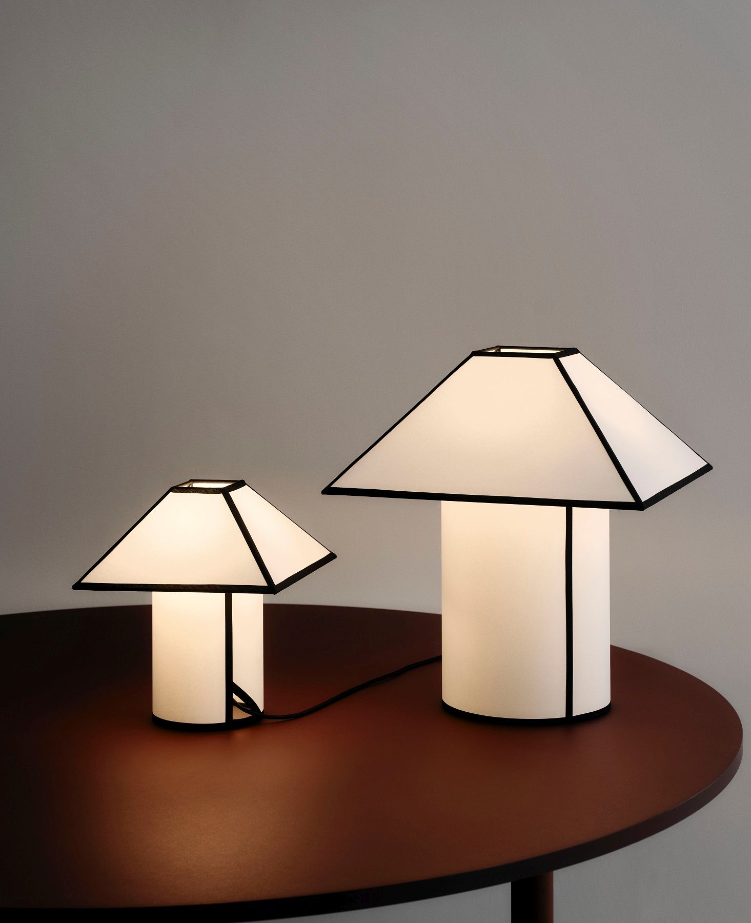 Zwei Ava Pyramid Tischlampen von Hay in verschiedenen Größen auf einem braunen Tisch.