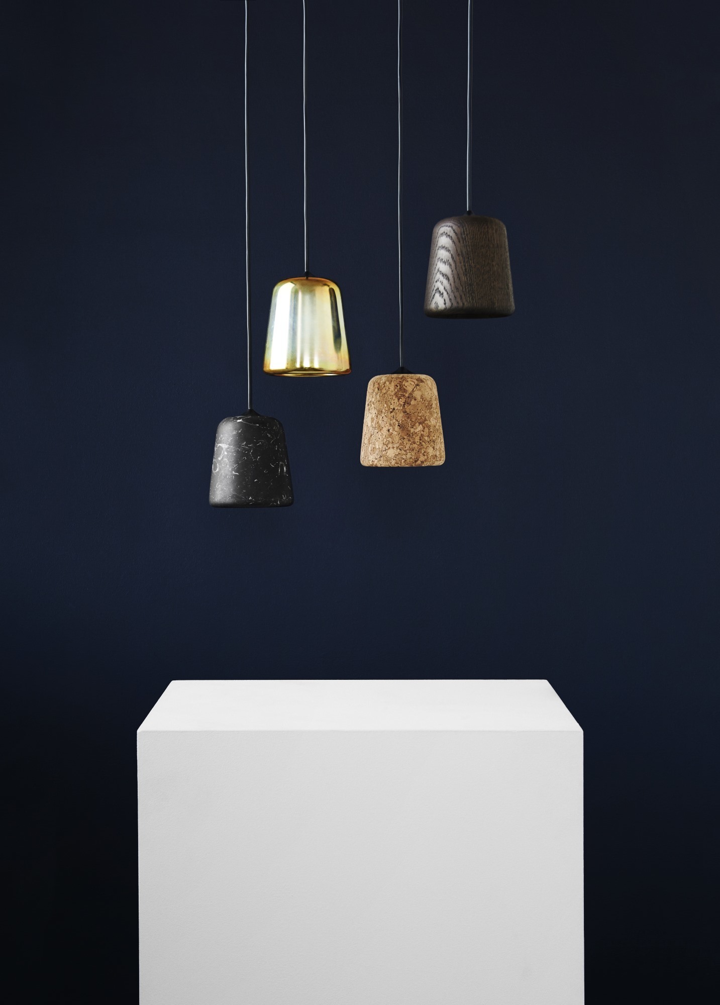 Material Pendant Pendelleuchten von New Works in Stahl, Kork, Marmor und Messing vor dunklem Hintergrund.