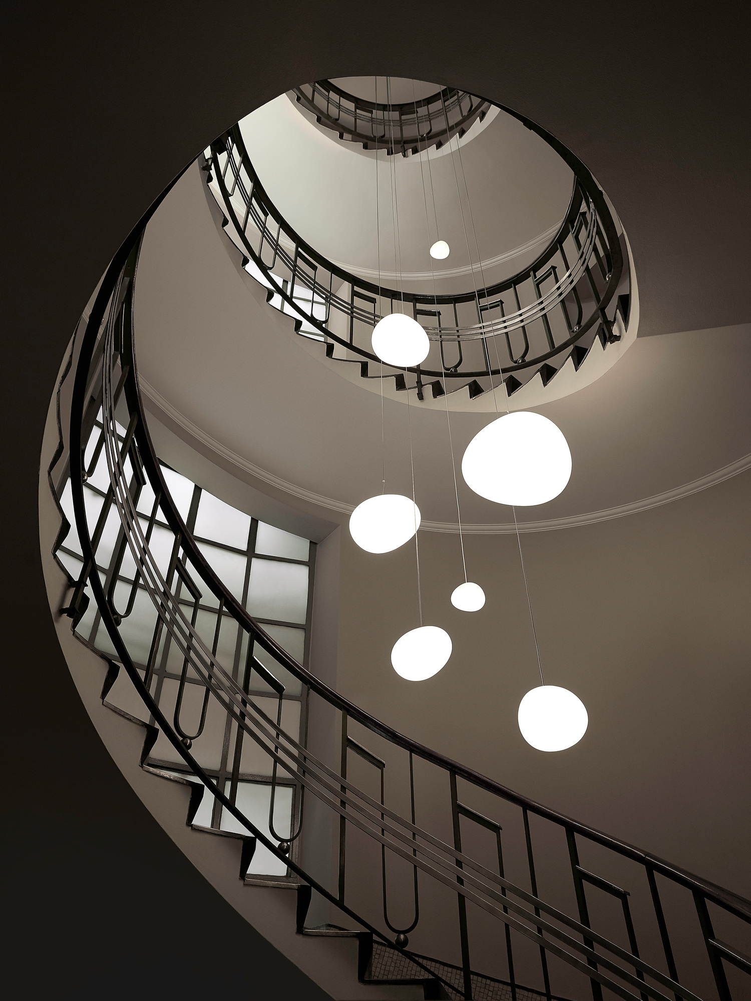 Gregg Pendelleuchte von Foscarini über einer Wendeltreppe, die von oben fotografiert wurde, mit mehreren runden Lampen.