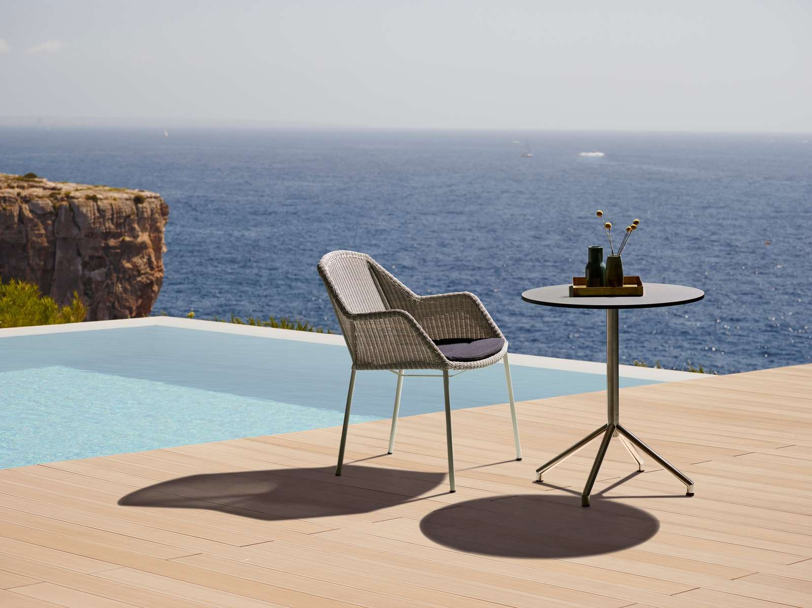Breeze Outdoor Stuhl von Cane-Line mit Vierfußgestell aus Aluminium und grauem Rattan vor Pool.