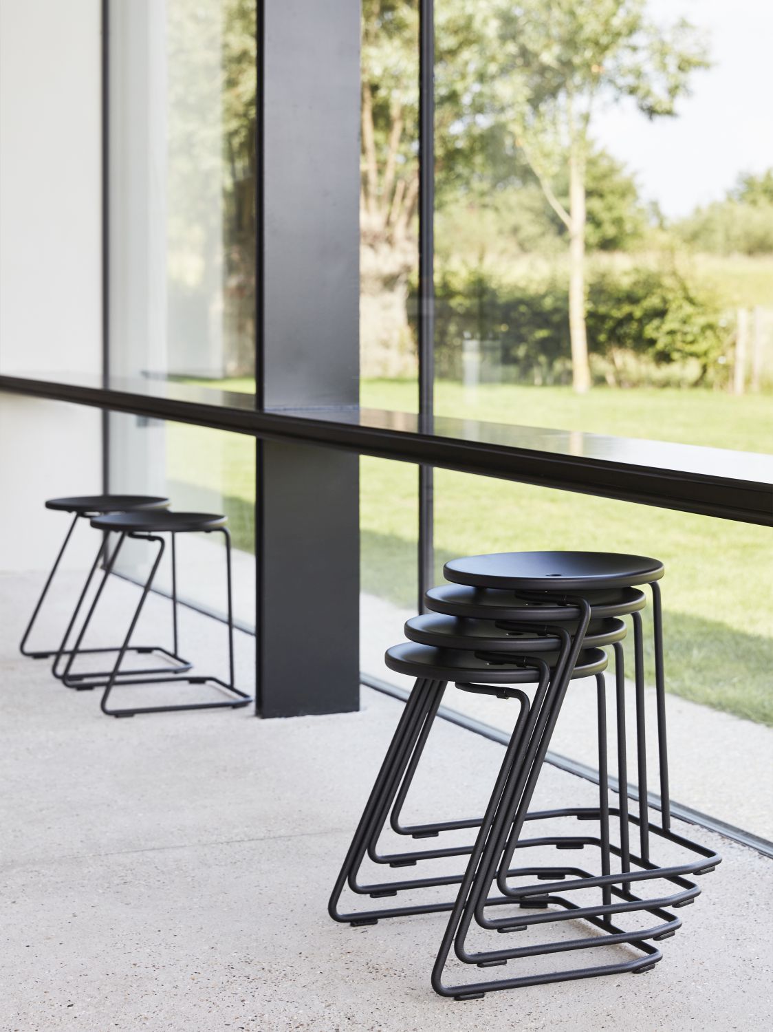 Schwarze Tiki Barhocker von Extremis für den Außenbereich, stapelbar und modern designt vor Fensterfront.
