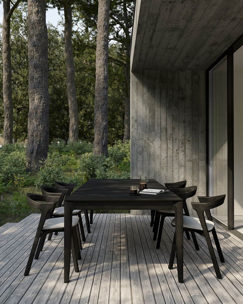 Bok Outdoor Esstisch aus Teakholz mit sechs Stühlen auf einer Holzterrasse vor Bäumen.