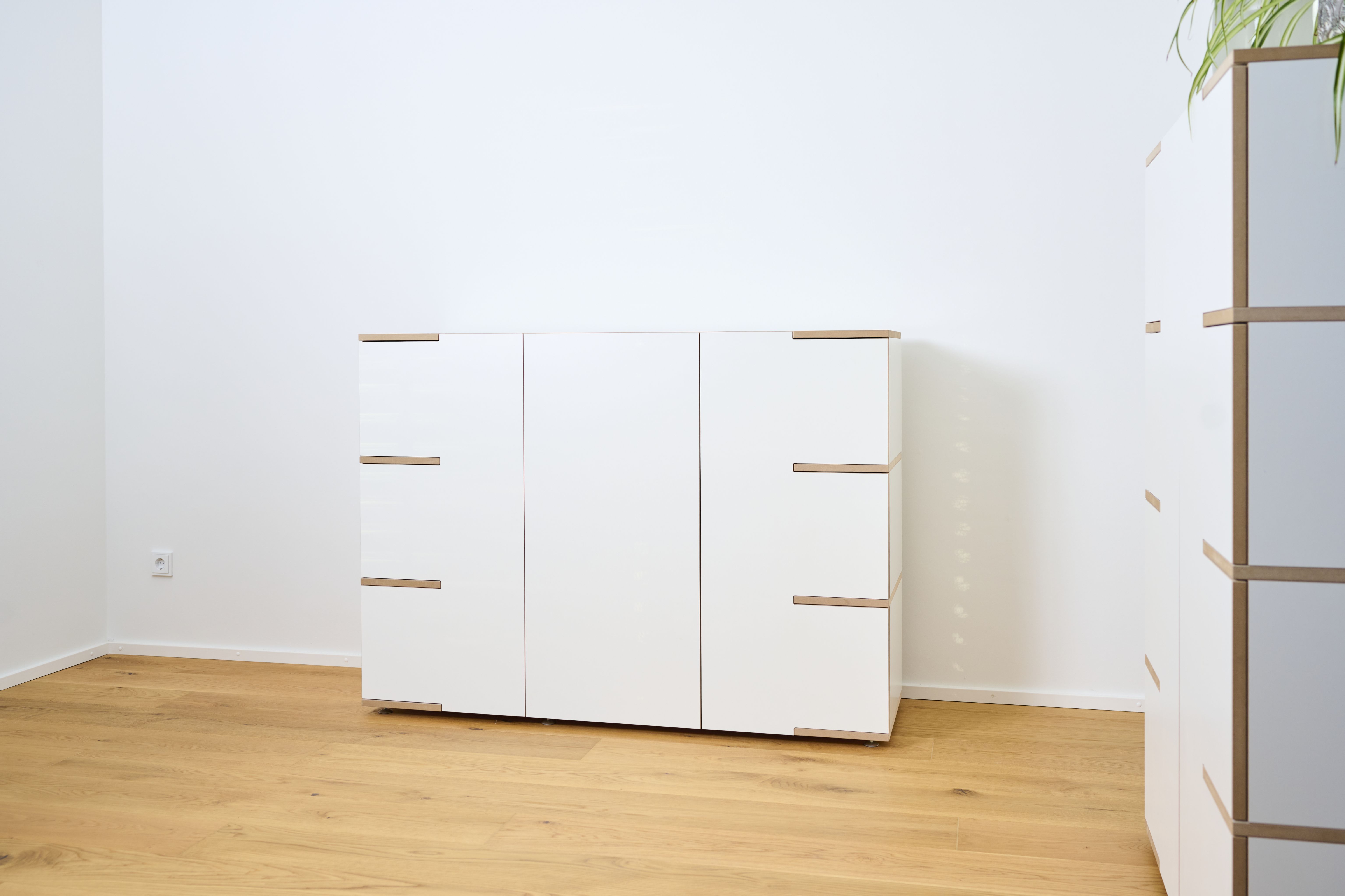 Tojo Stau Sideboard aus weißem Holz mit drei Türen und hellen Holzdetails auf Holzboden.