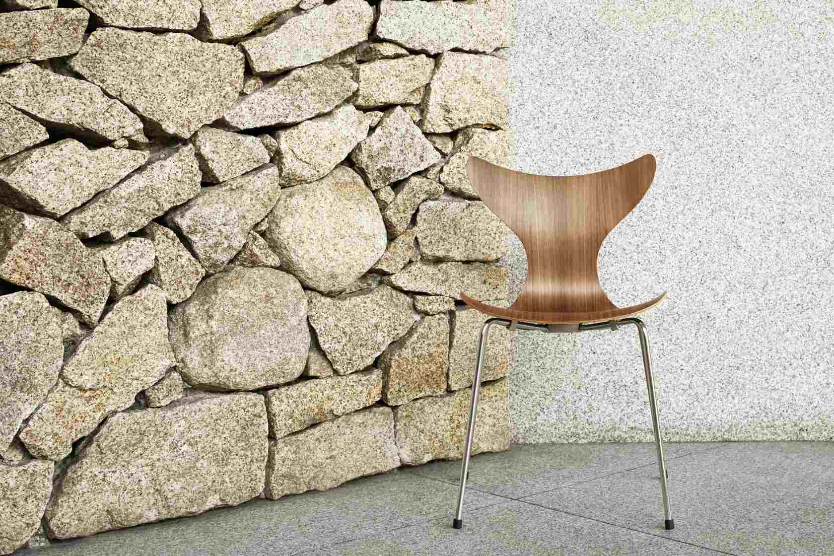Fritz Hansen Lily Stuhl 3108 aus Holz mit Stahlbeinen vor Steinwand und Putz.