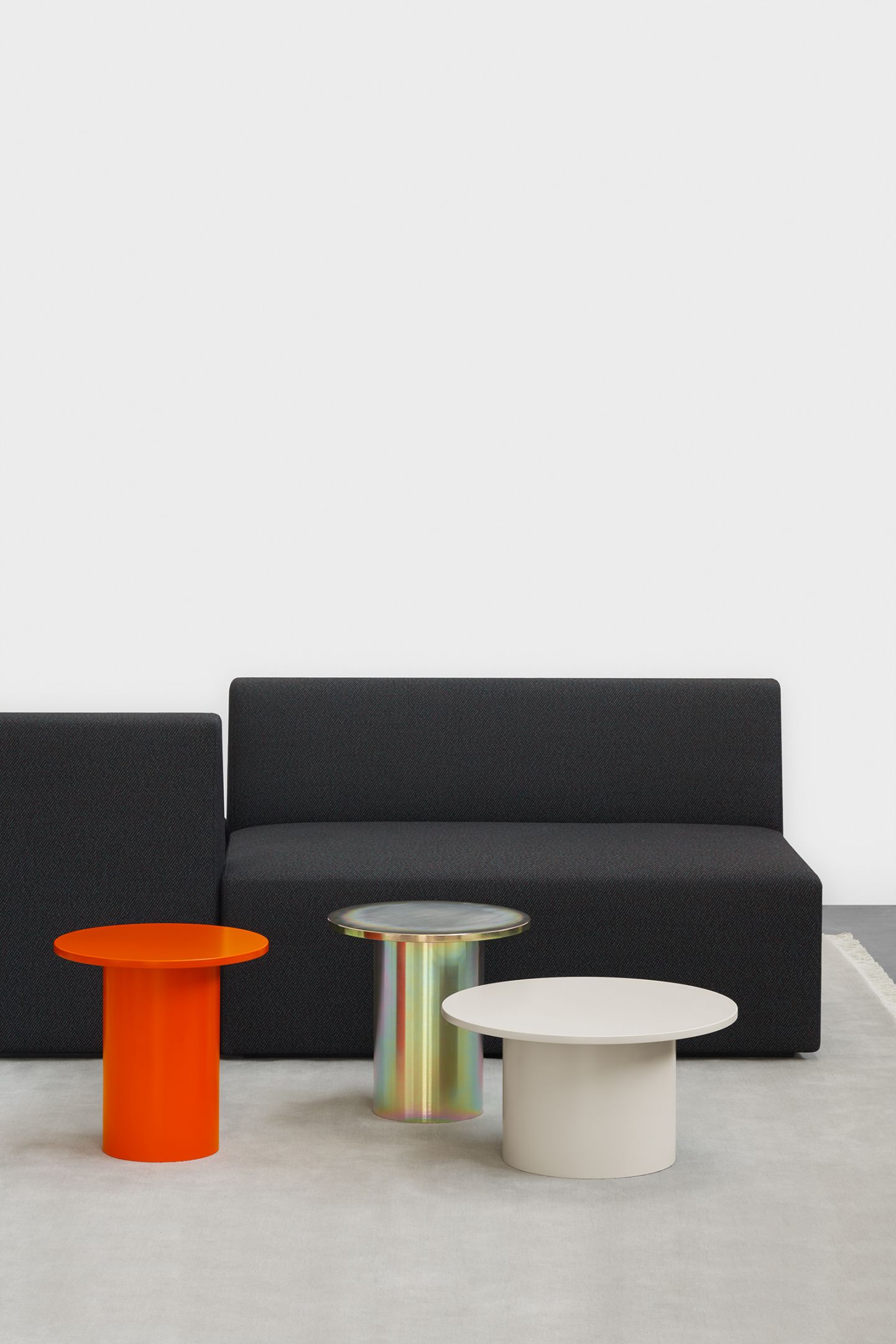 Enoki Beistelltische von e15 in Orange, Beige und irisierend vor einem schwarzen Sofa.