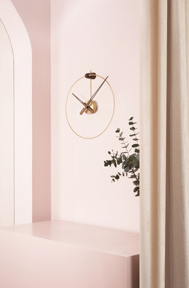 Elegante Micro Anda Clock Wanduhr von nomon in Schwarz und Gold vor rosa Wand.
